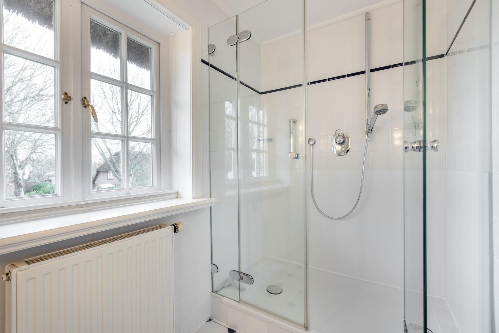 Shower cabin with glass enclosure and window overlooking outside.