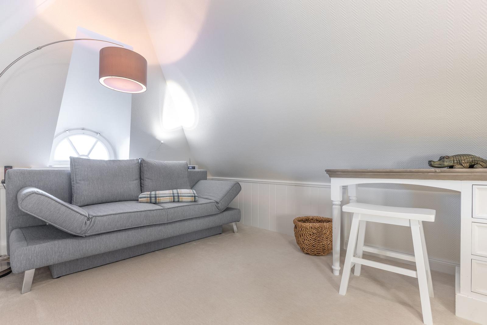 A room with gray sofa, desk and standing lamp under a vaulted ceiling.