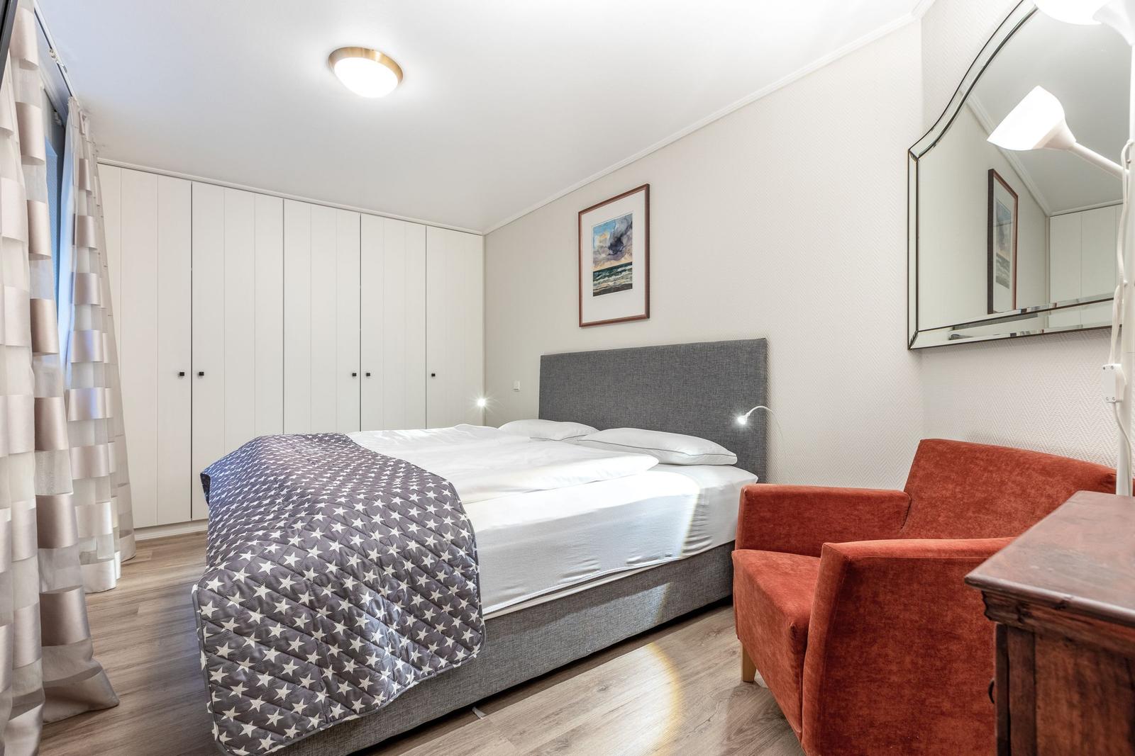 Bedroom with bed, wardrobe, armchair, and mirror.