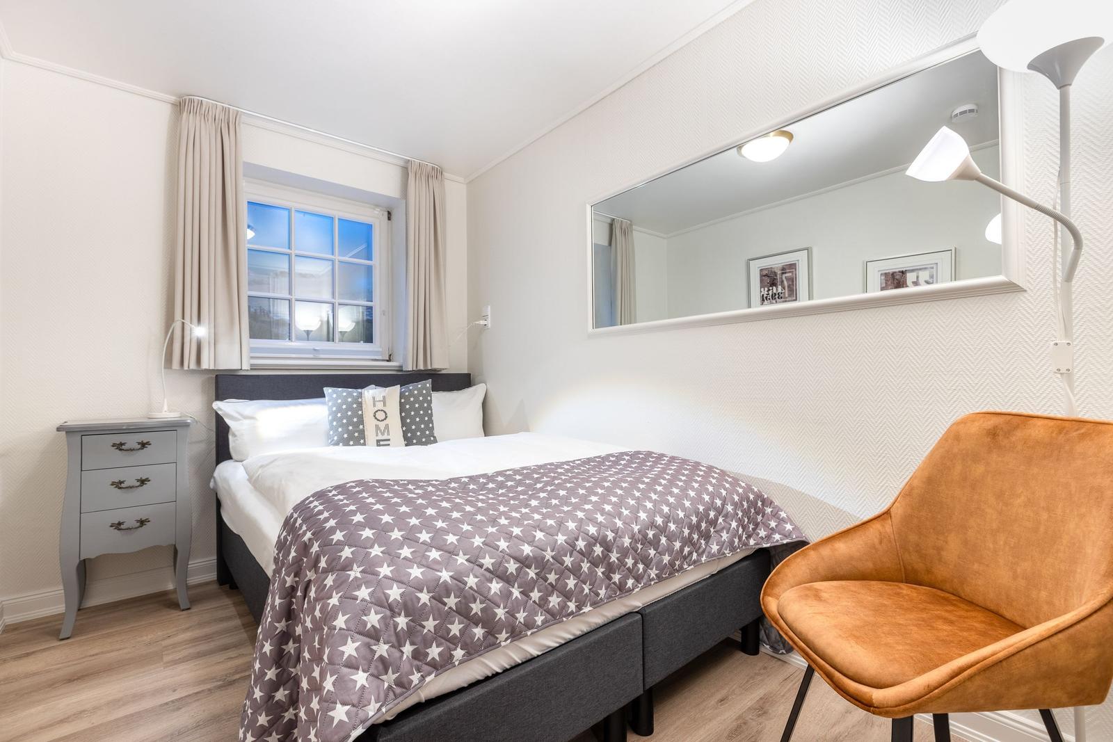 Bedroom with bed, nightstand, mirror, and chair.