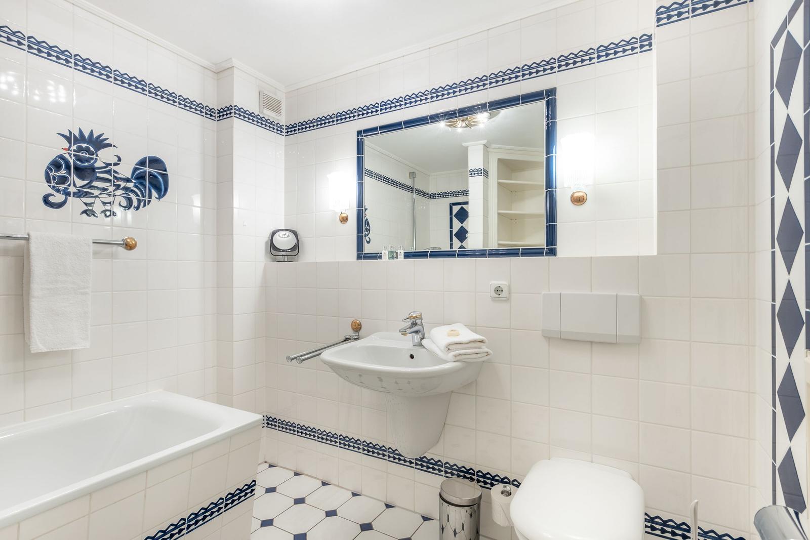 Bathroom with bathtub, sink, and toilet. Blue tile trim and mirror.