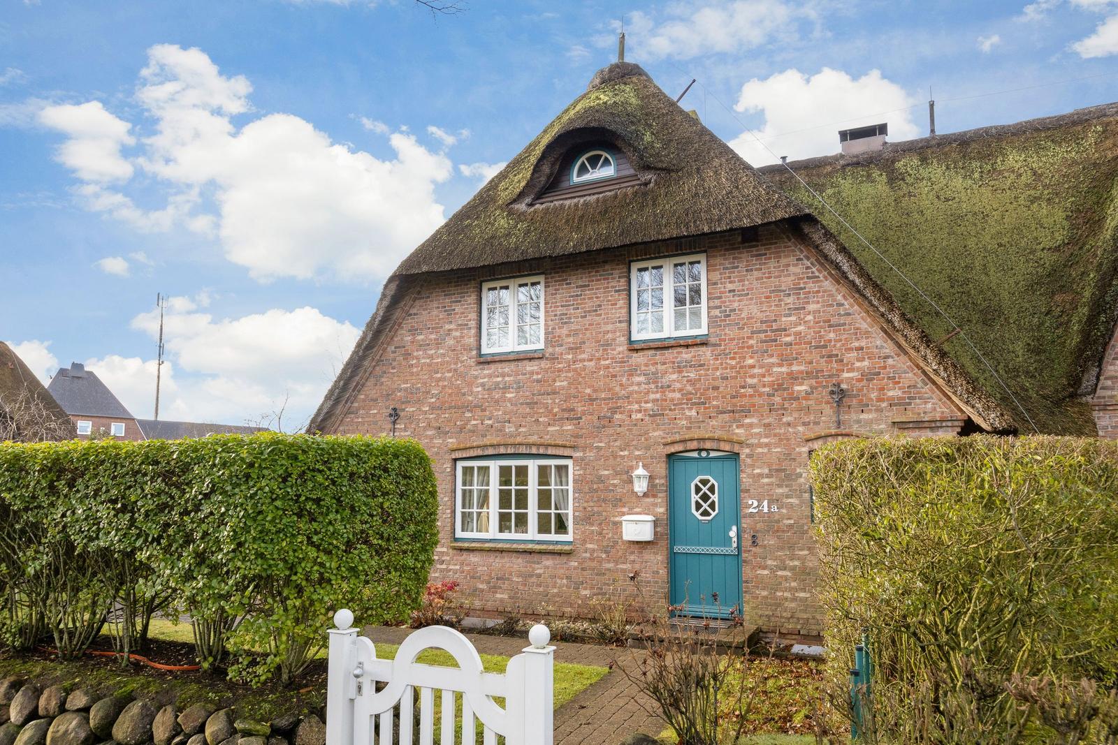 House with thatched roof, green door, and hedges. Number 24a.