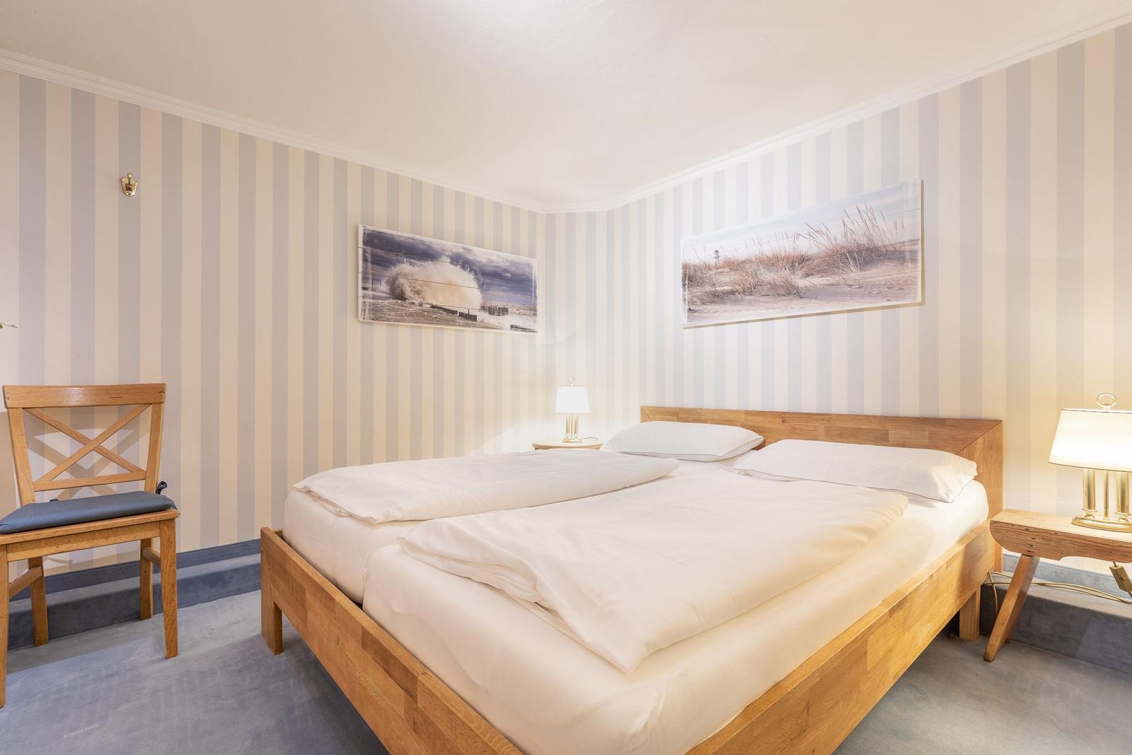 A bedroom with wooden bed, striped walls, and two wall pictures.