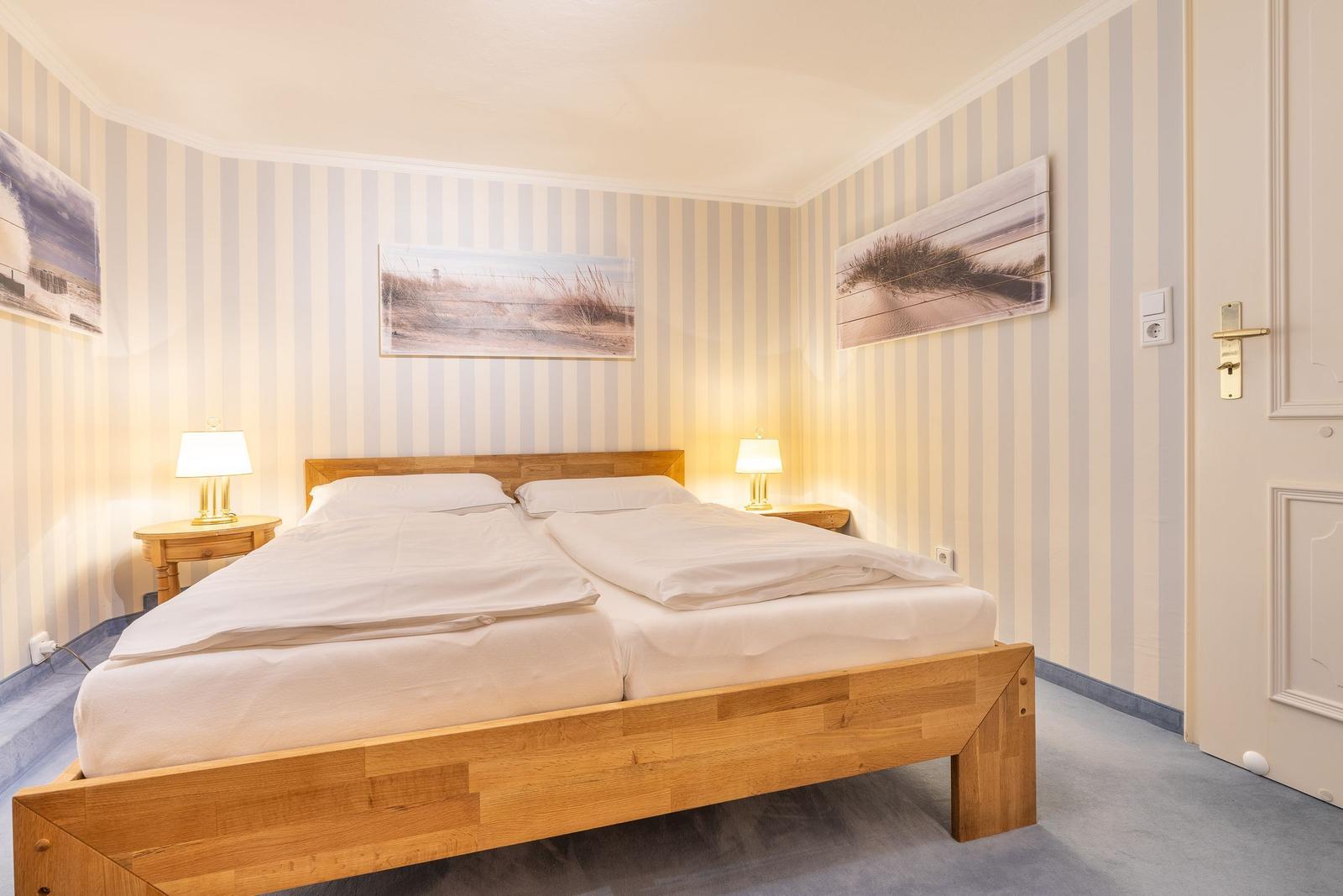 Bedroom with wooden bed, striped walls, and nightstands with lamps.