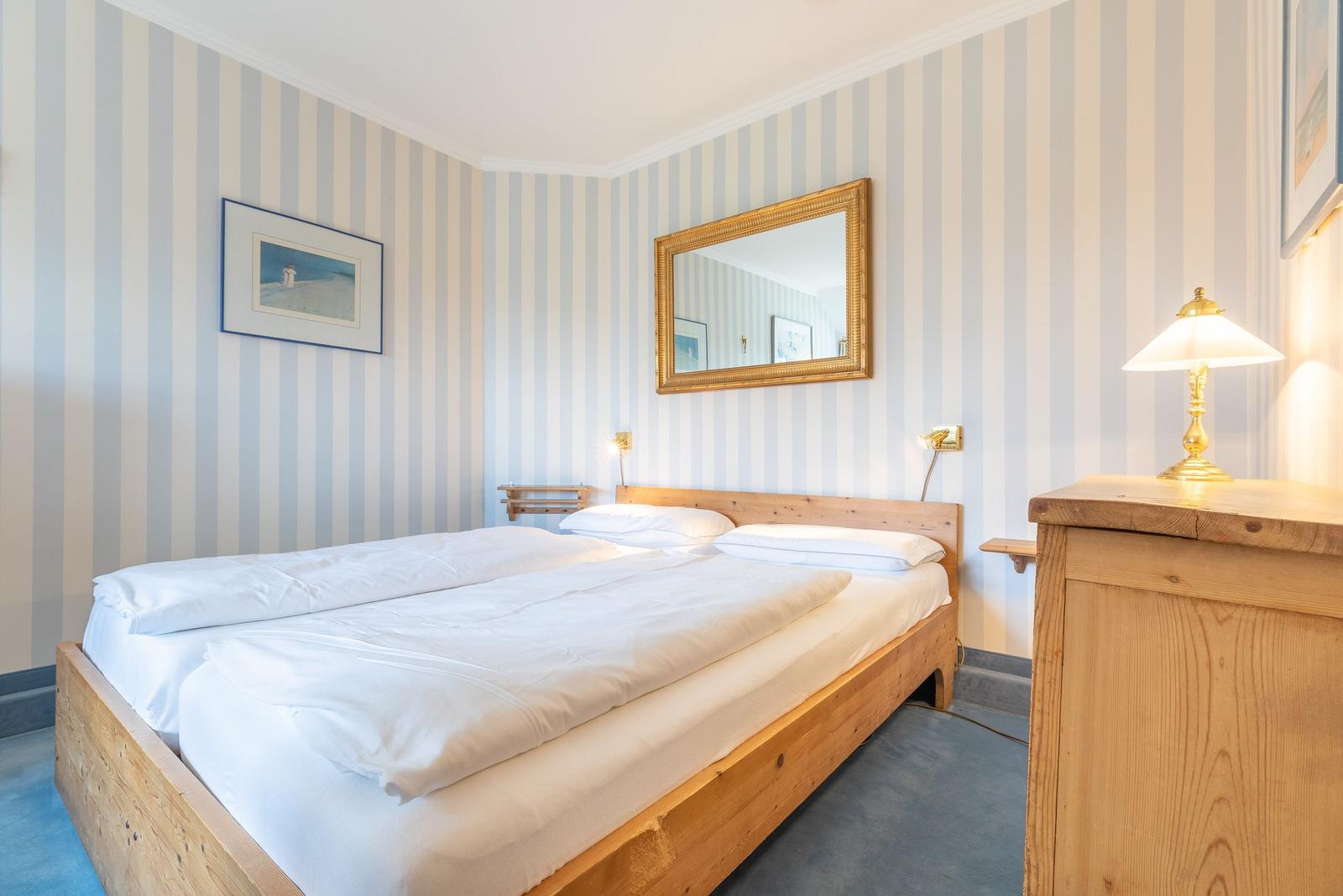 Bedroom with wooden bed, striped wallpaper, and gold mirror.