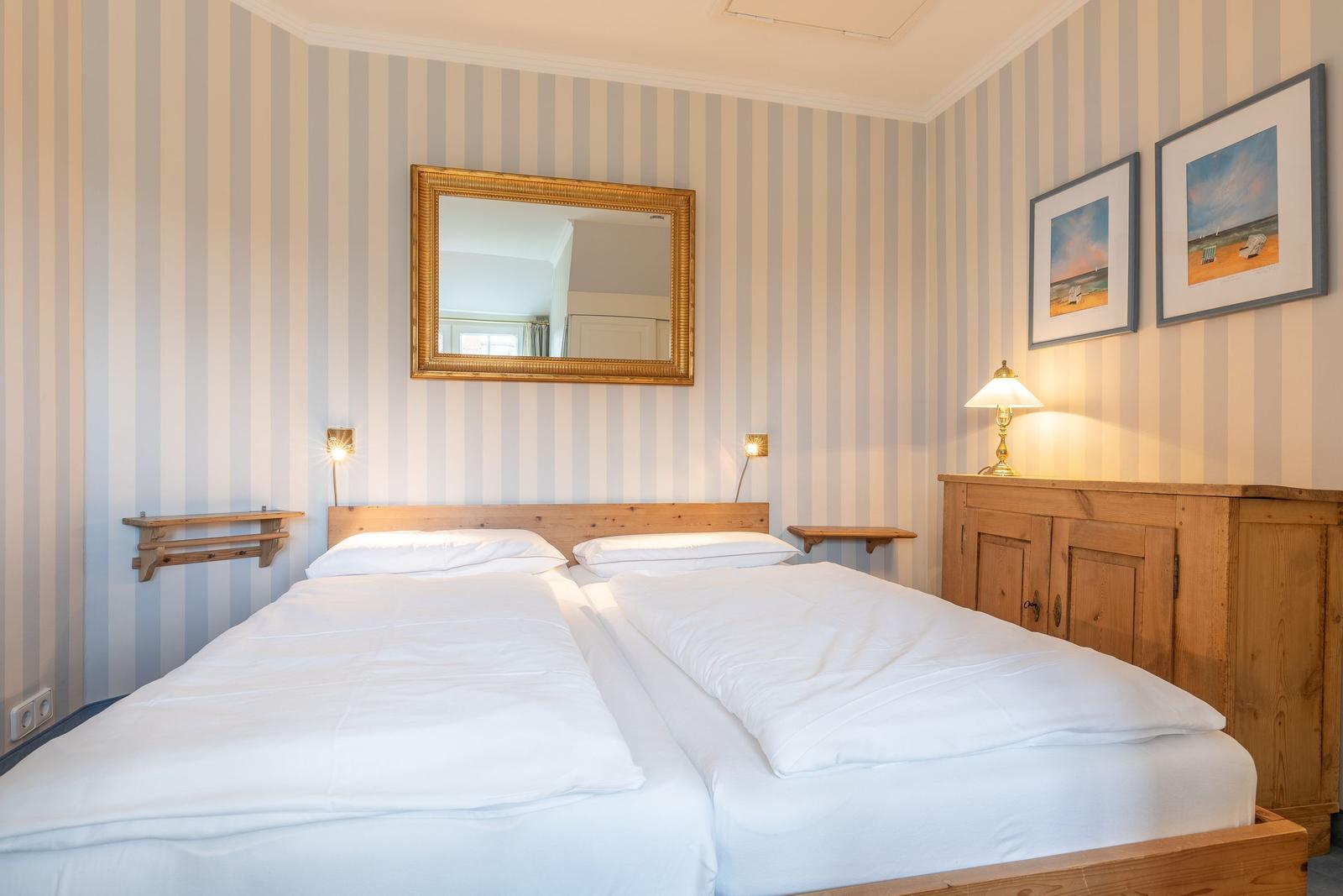 Two beds with white bedding, wooden furniture, and striped walls.