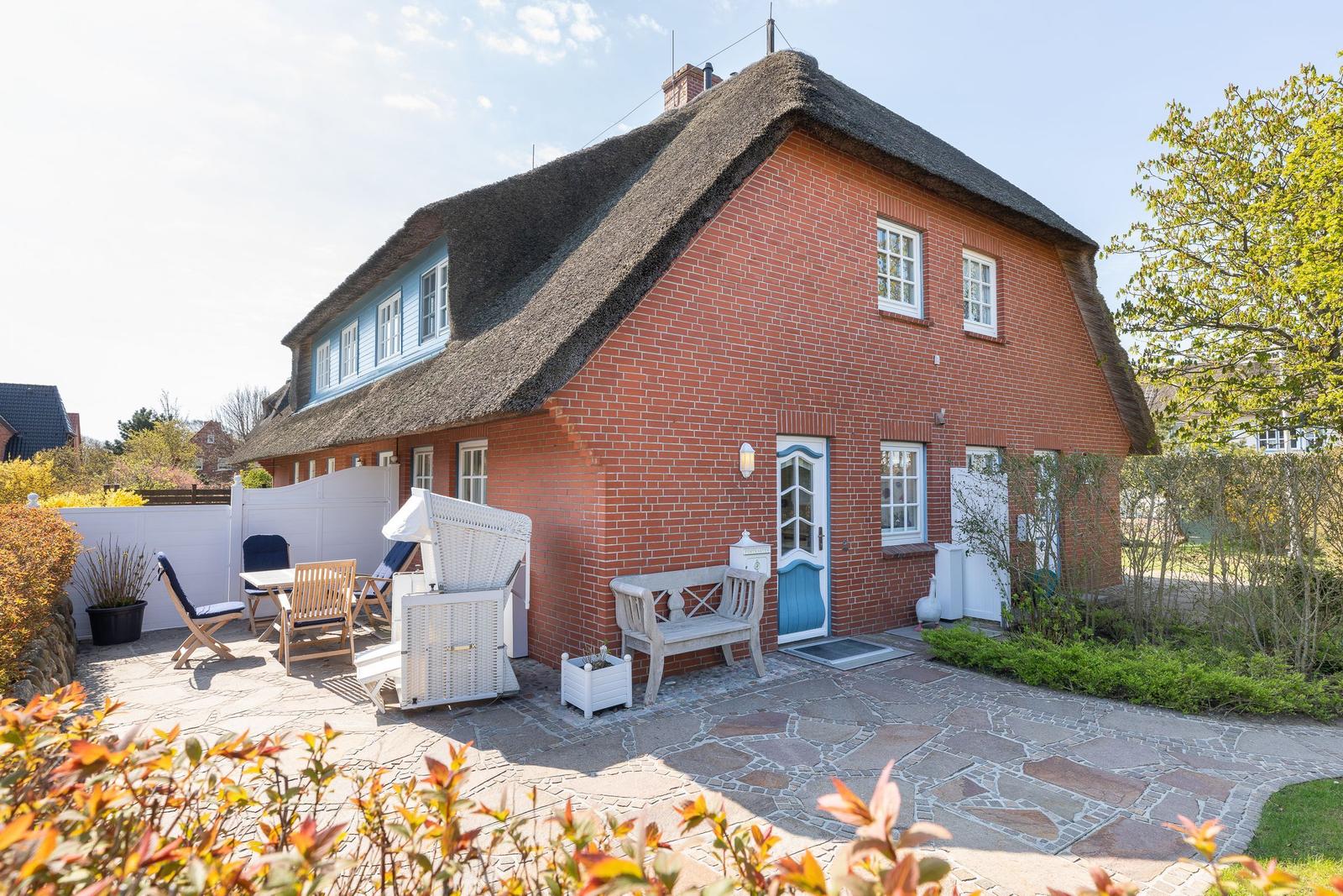 Red brick house with thatched roof and terrace with garden furniture.