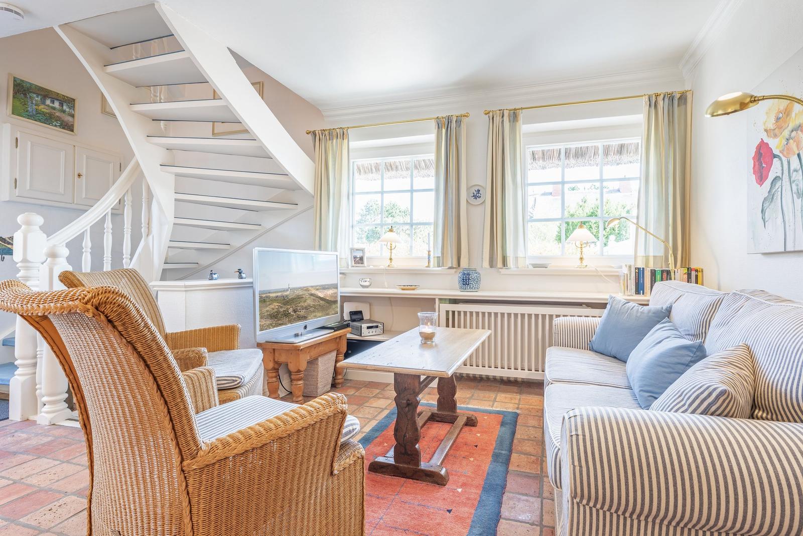 Living room with sofa, armchairs, TV, and staircase. Windows with curtains and rug.