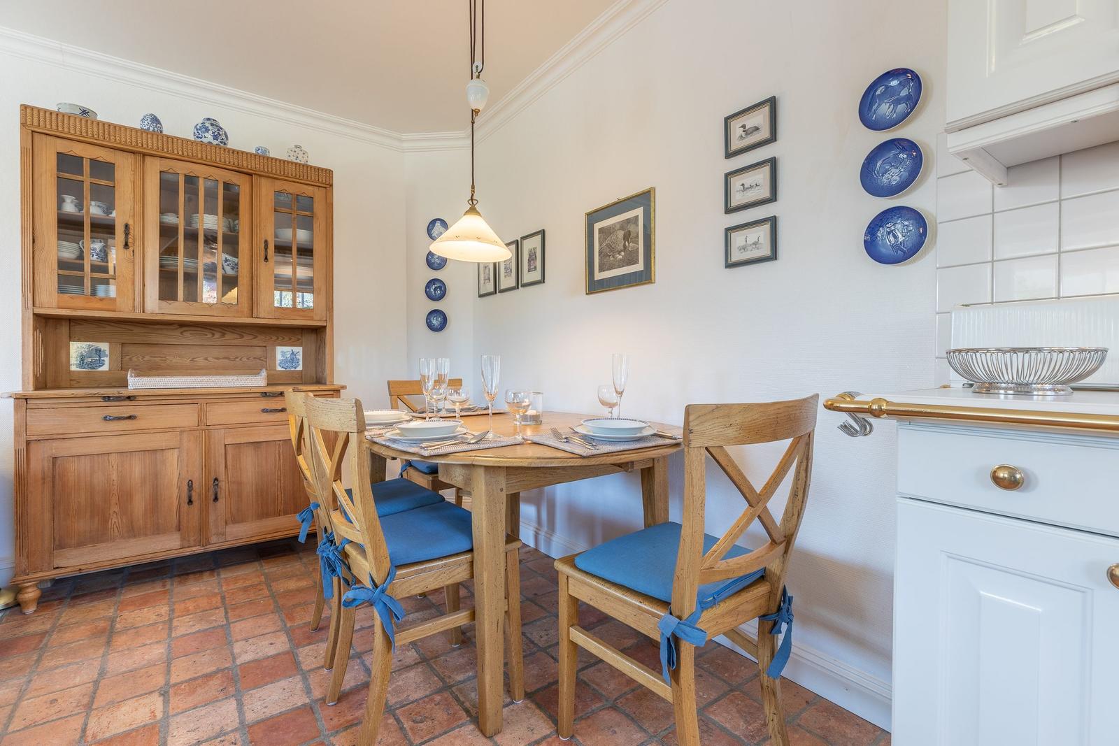 Dining room with wooden table, chairs, and kitchen area. Wall with pictures and blue plates.