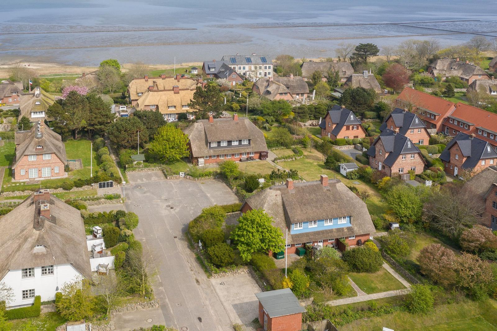 Village with thatched houses and green gardens by the water.