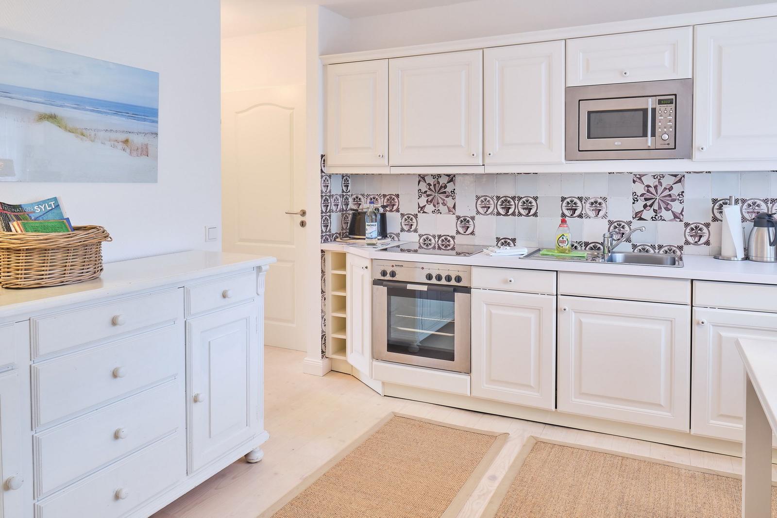 Küche mit weißen Schränken, Mikrowelle und Backofen. Fliesenwand und Holzboden.