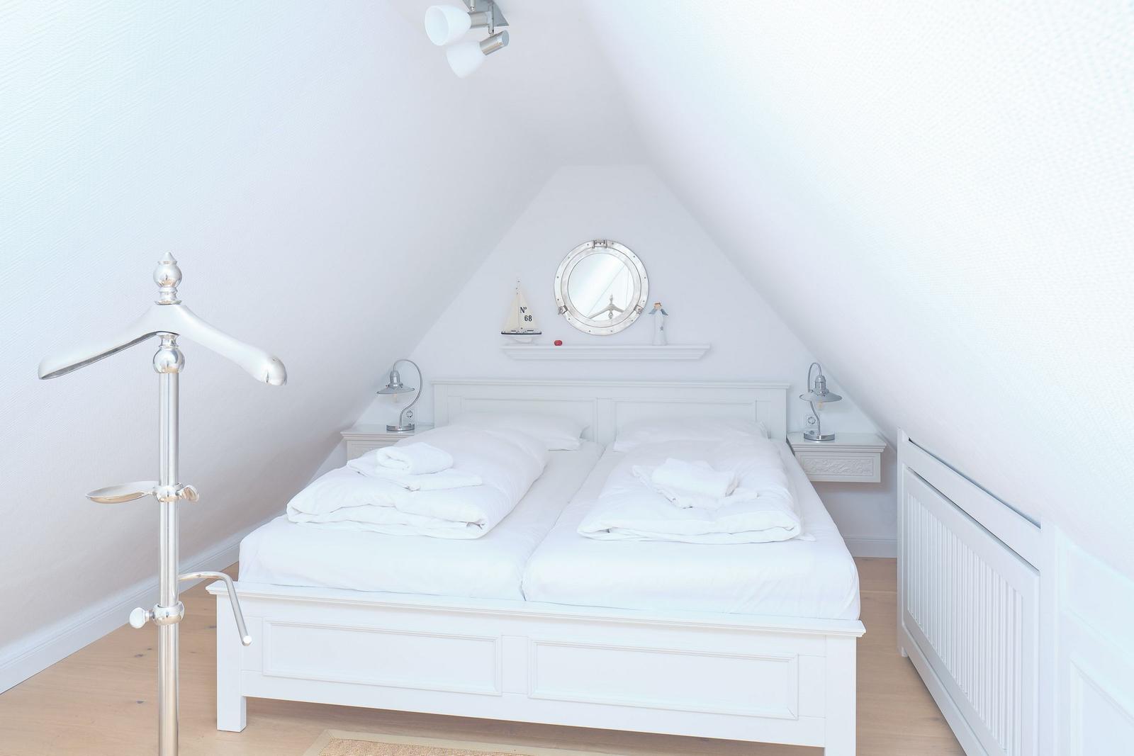 Ein Schlafzimmer mit Doppelbett, weißen Wänden und einem Kissenständer.
