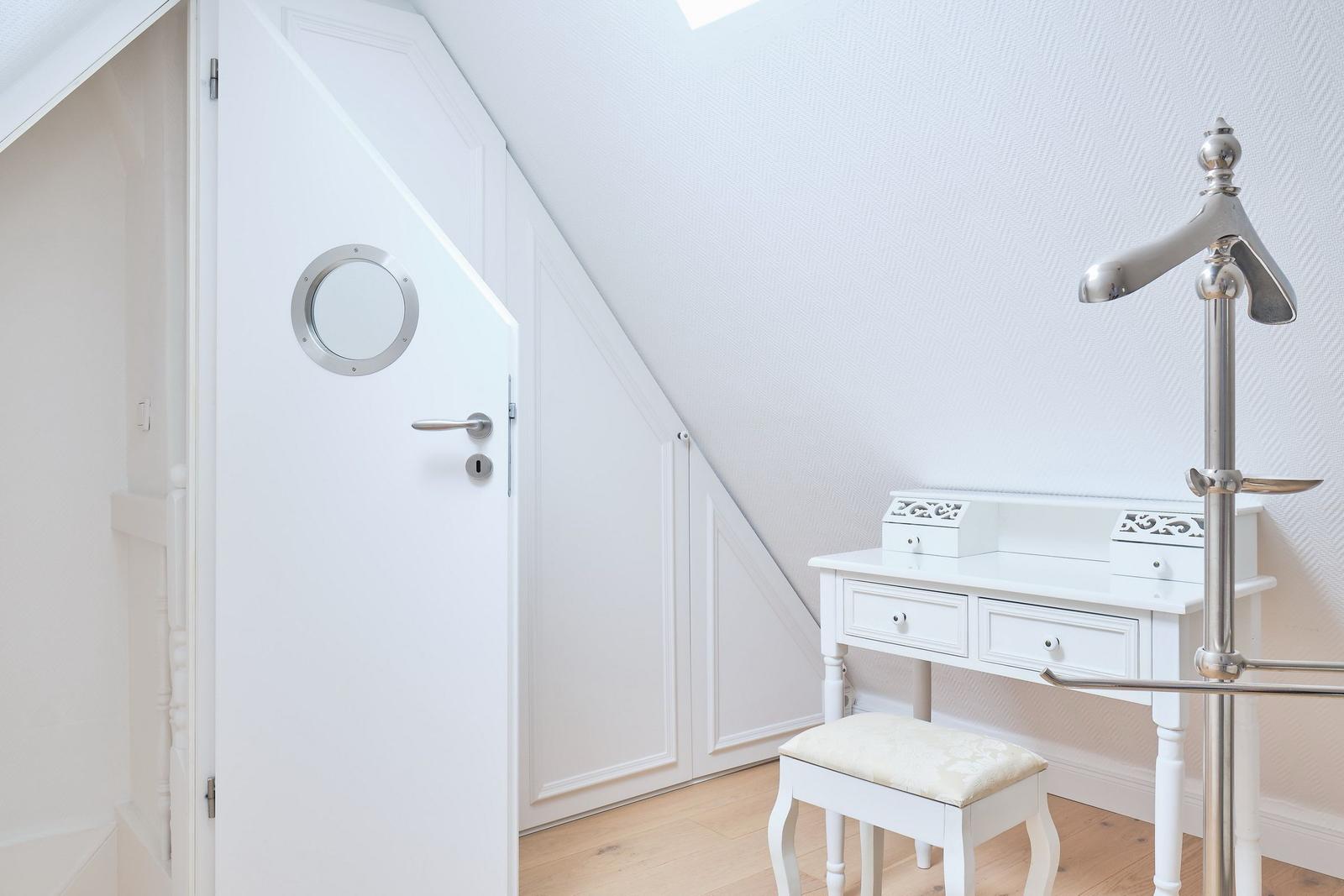Schlafzimmer mit weißem Schrank, Schreibtisch und Stuhl unter schräger Decke.
