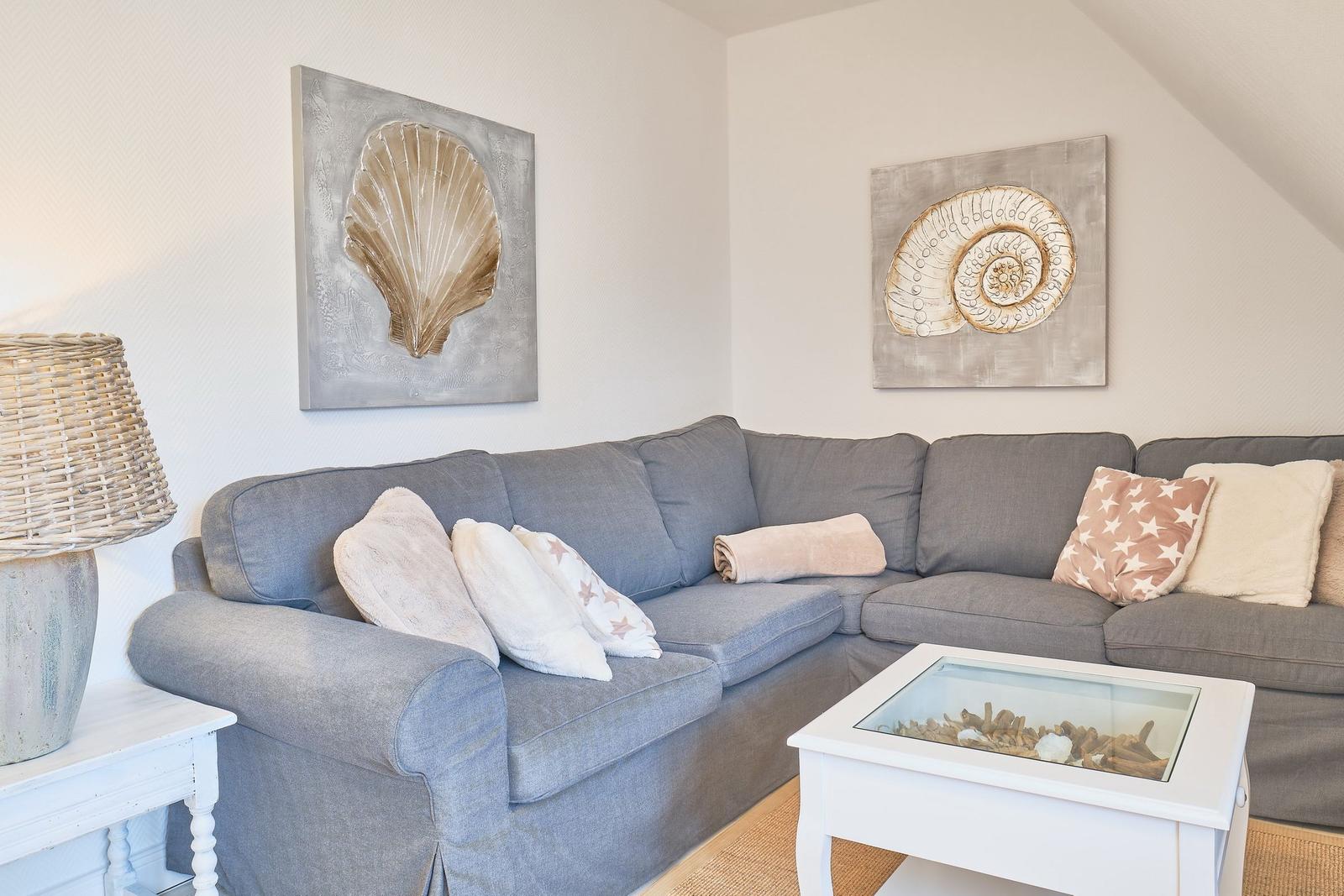Grauer Sofa mit Kissen und Wandbildern von Muscheln.