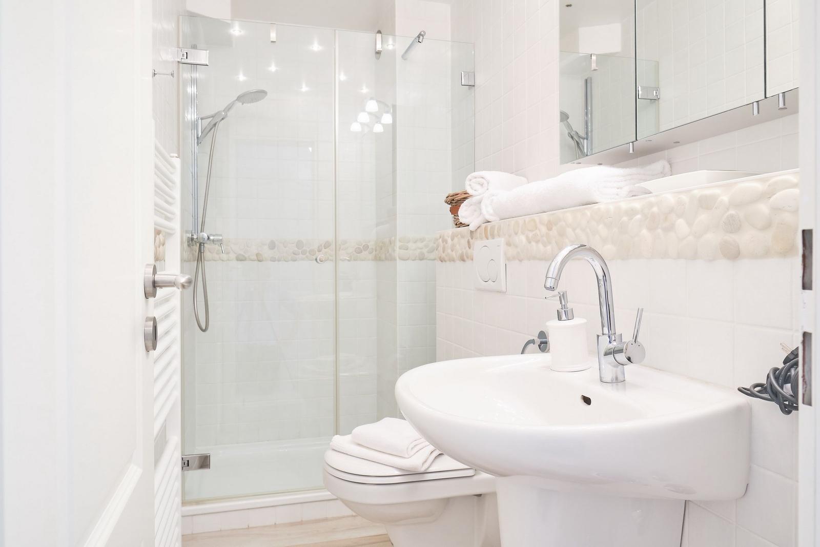 Bad mit Dusche, Waschbecken und Toilette. Steinverkleidung und Spiegel.