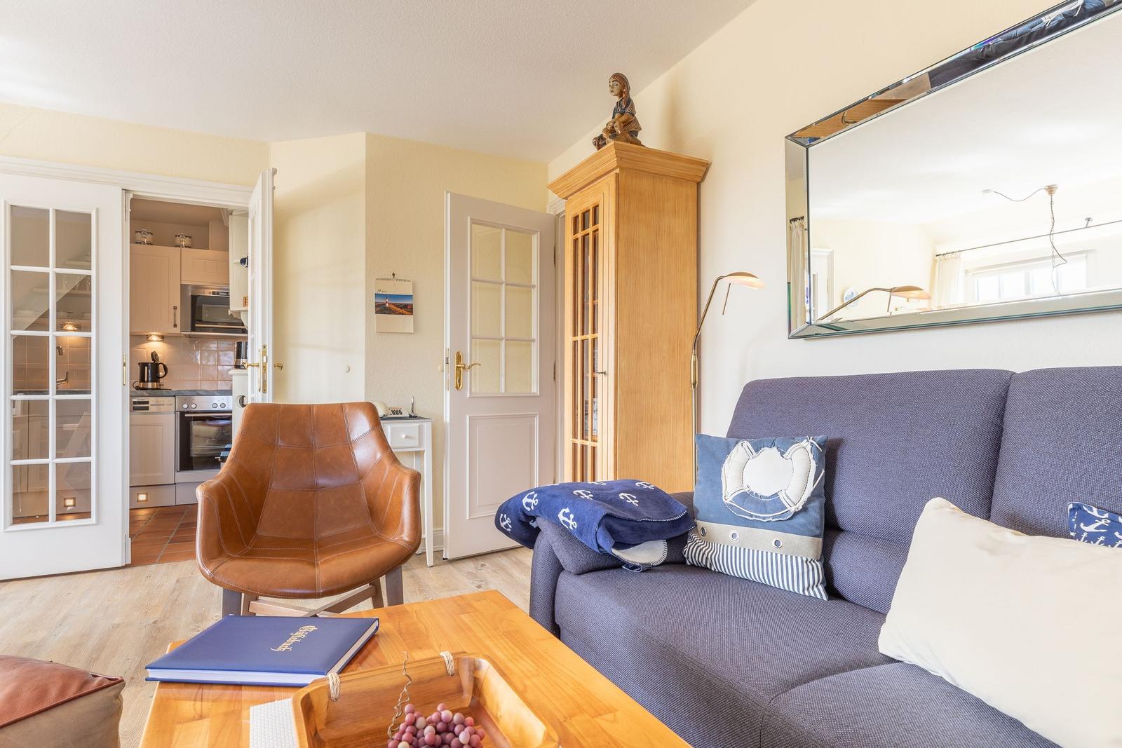 Living room with sofa, chair, and kitchen area in the background.