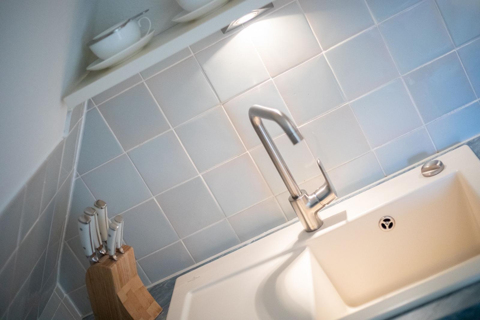 Kitchen faucet with cutting board and knives against gray tiled wall