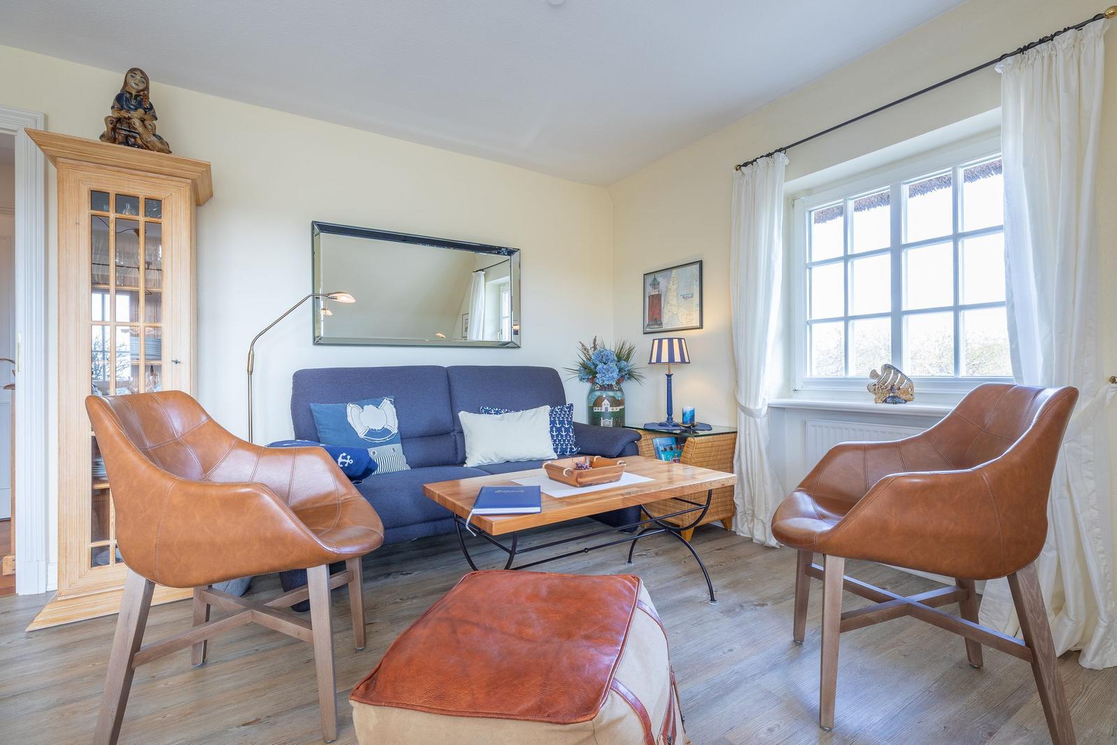 A living room with blue sofa, two brown leather chairs, and wooden floor.