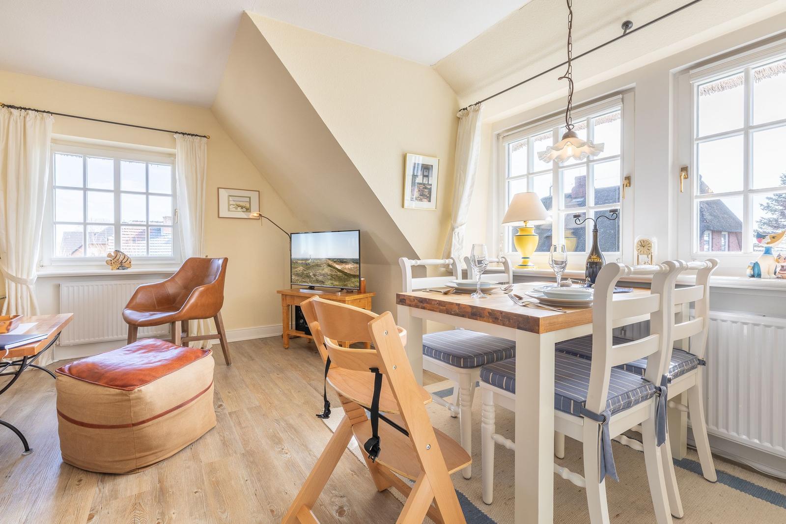 Dining room with table, chairs, and windows. A TV and a chair are also visible.