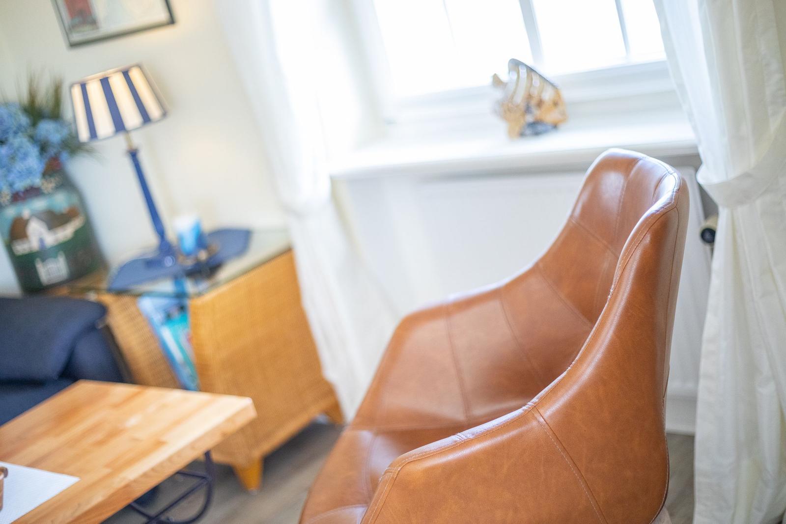 A brown leather sofa in front of a window with white curtains.