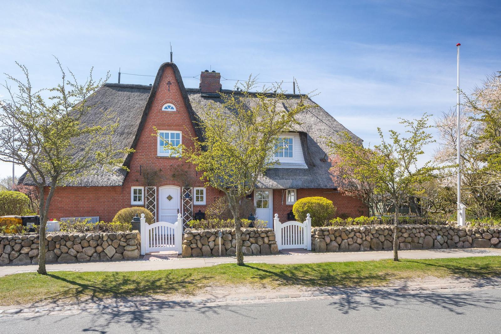 Red brick house with thatched roof and white gate