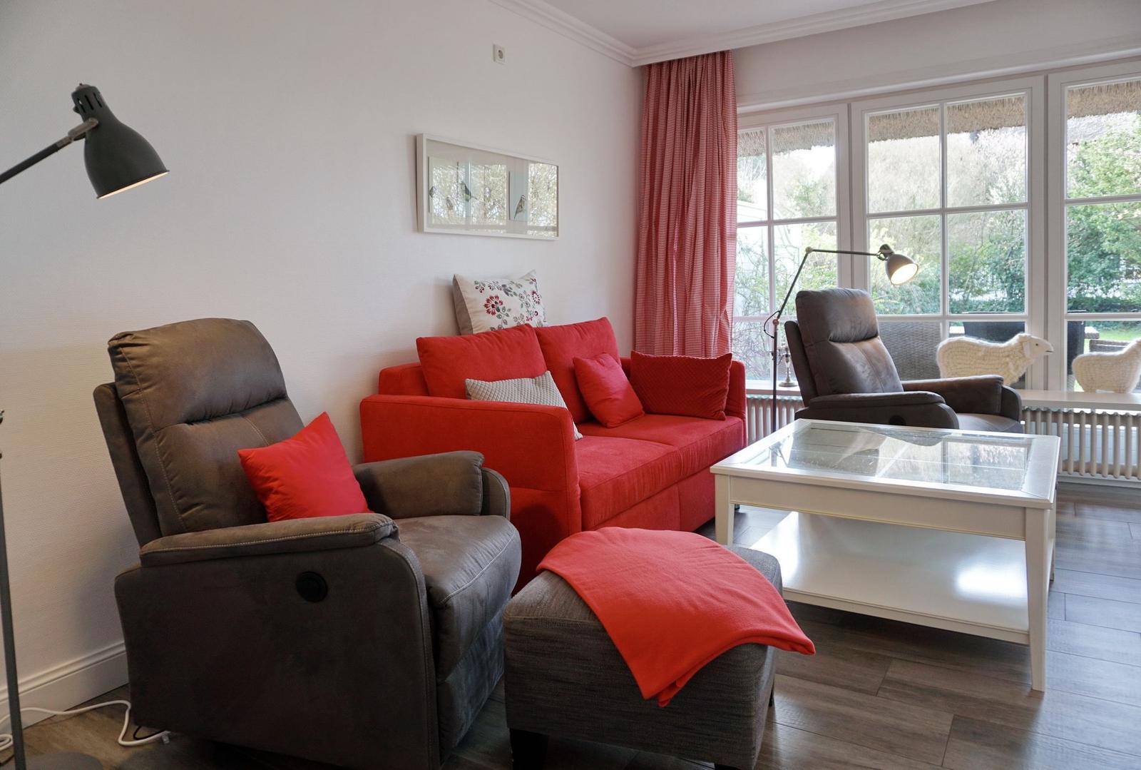 Ein Wohnzimmer mit rotem Sofa, grauen Sesseln und einem Glas-Tisch.