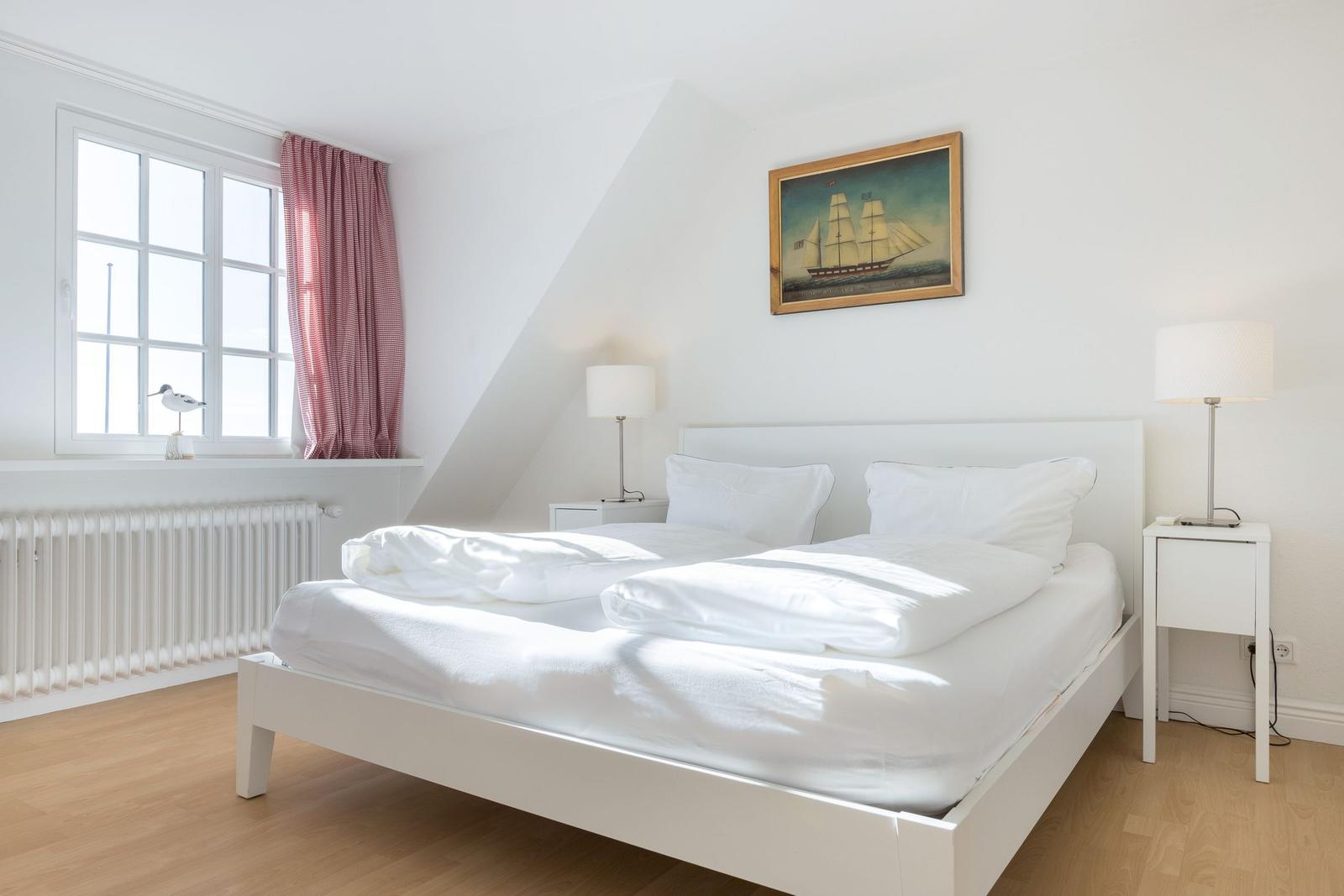 Schlafzimmer mit weißem Bett, Fenster und Bild an der Wand.