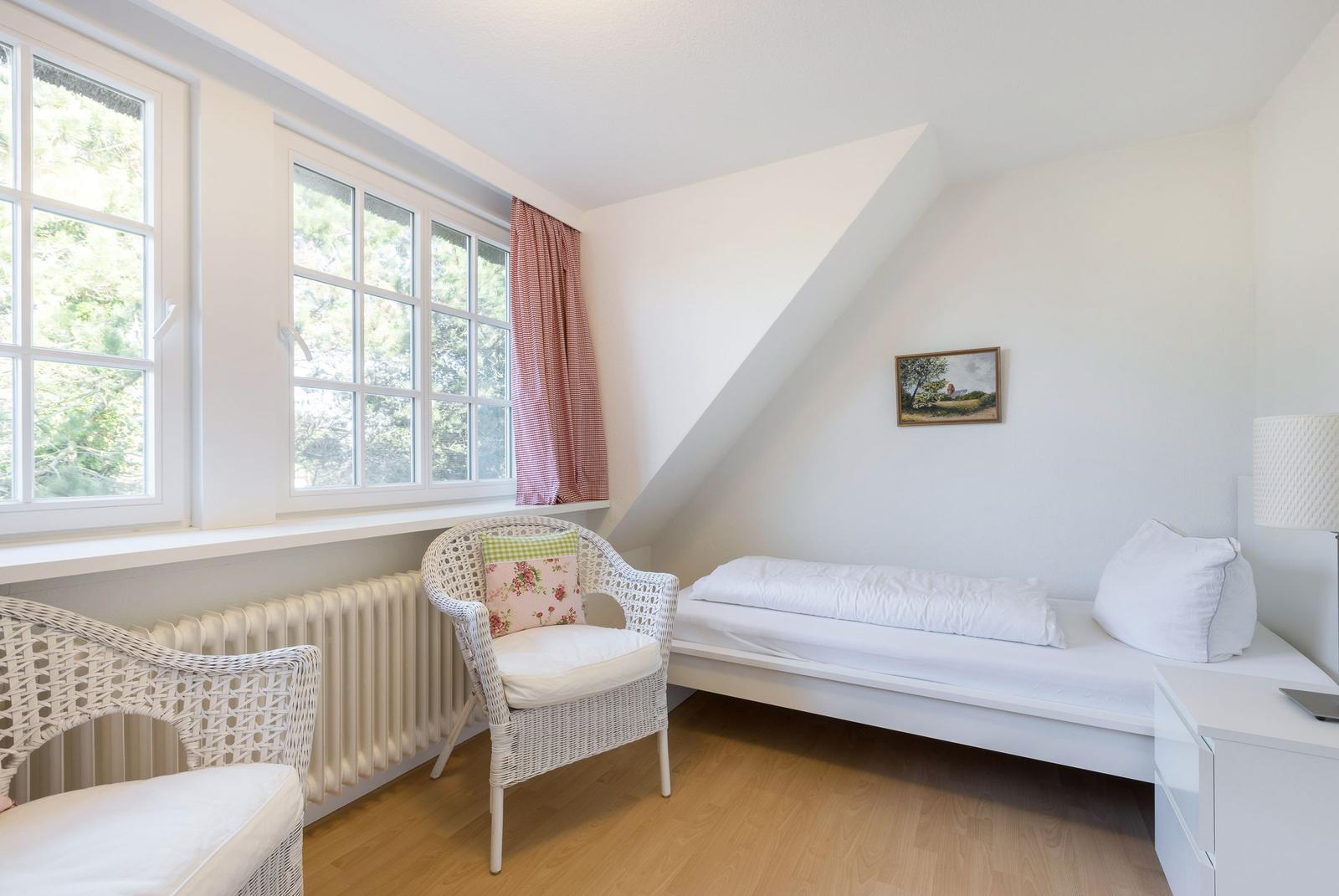 Ein Schlafzimmer mit Dachschrägen, Fenster, Bett und Stühlen.