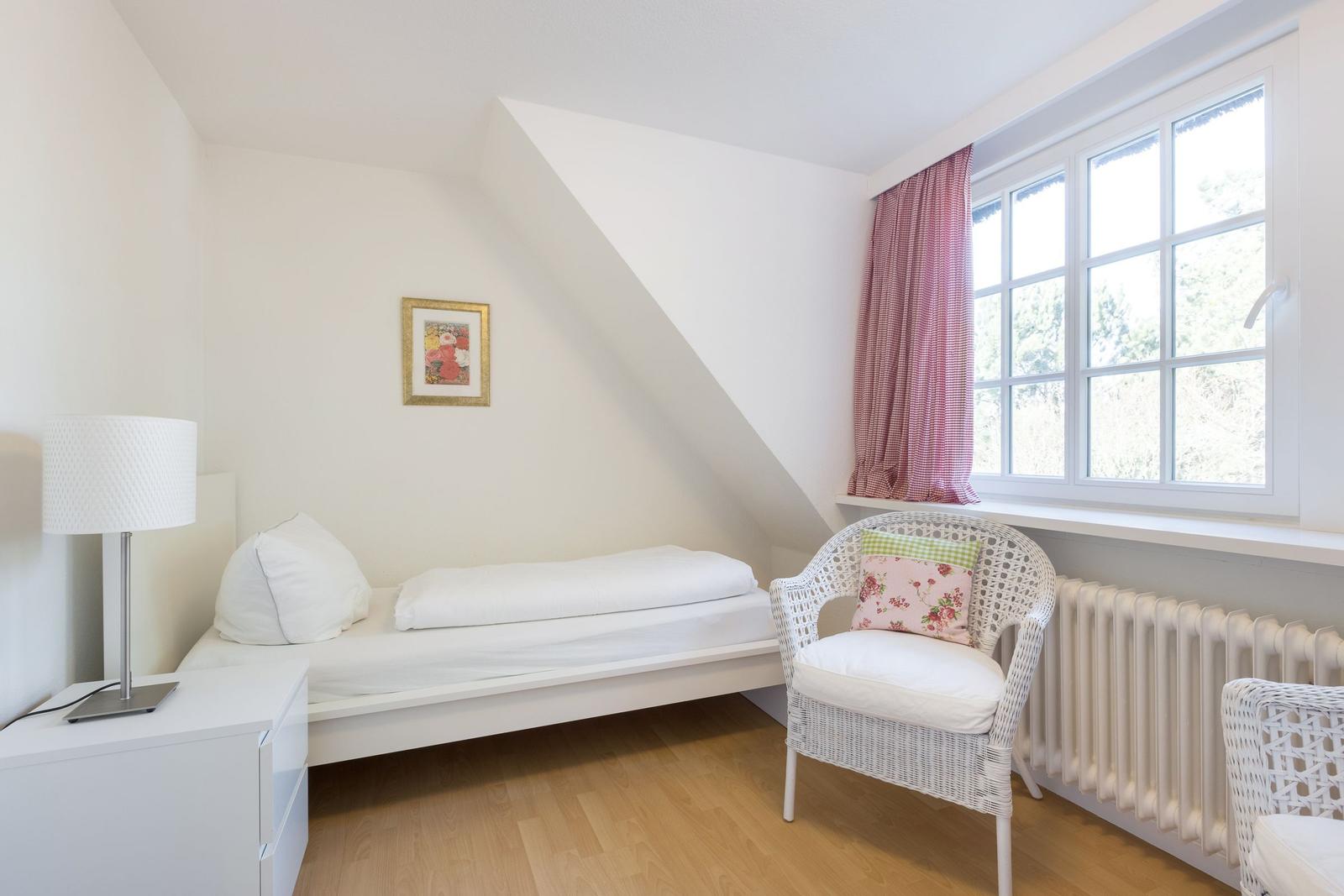 Ein Schlafzimmer mit weißem Bett, Stuhl und Fenster mit Vorhang.