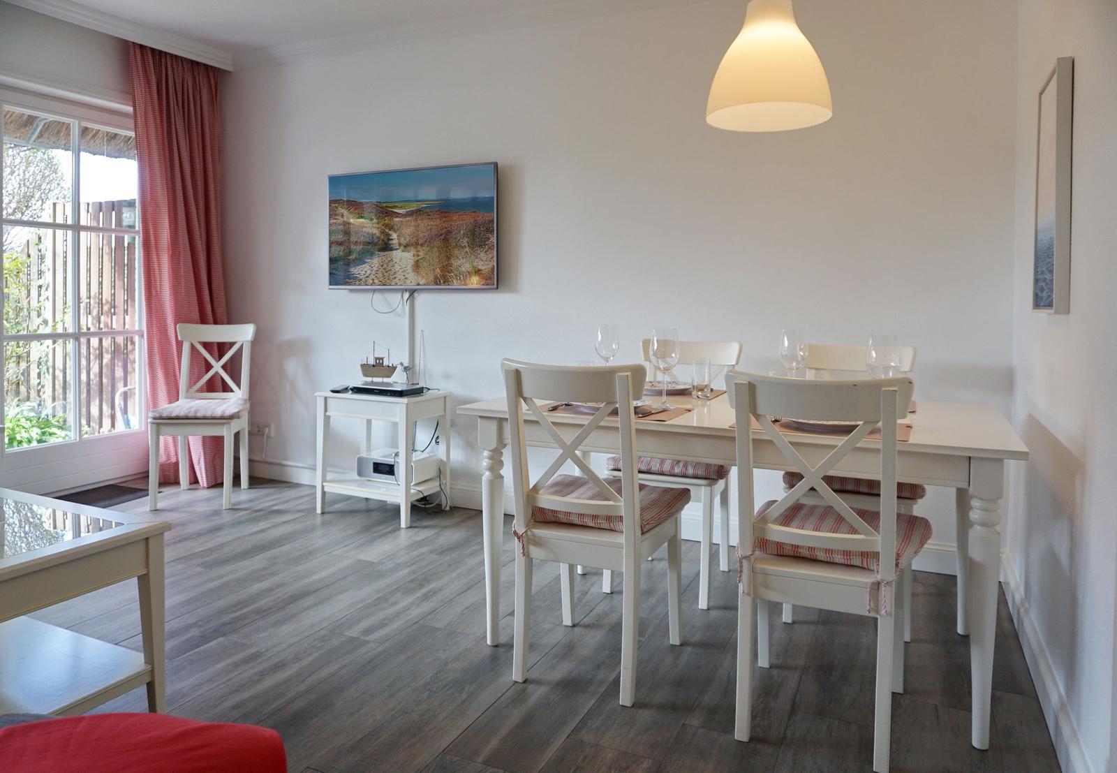 Esszimmer mit weißem Tisch, Stühlen und Fernseher an der Wand.