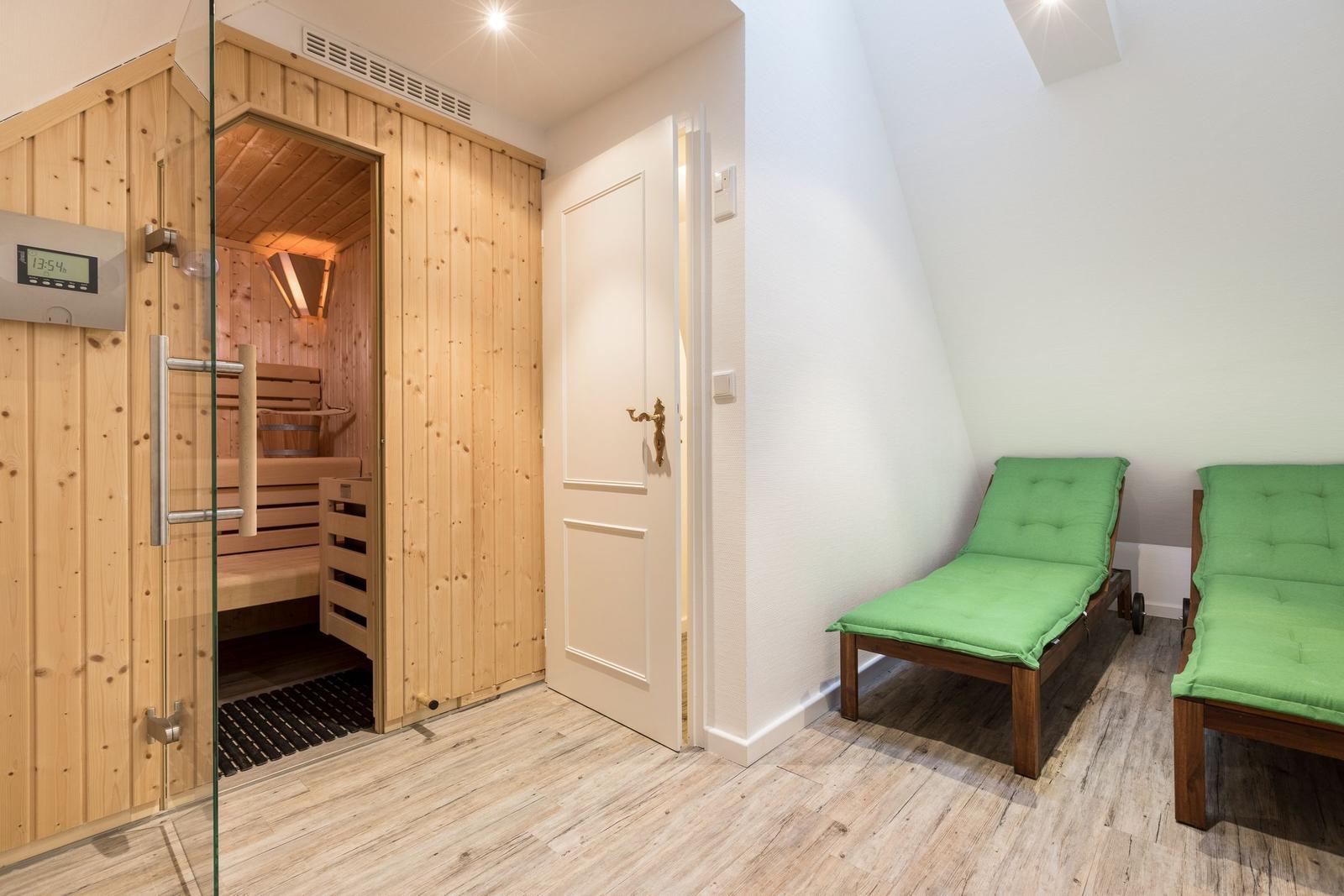 Sauna mit Glaswand und zwei grünen Liegen im Dachgeschoss.