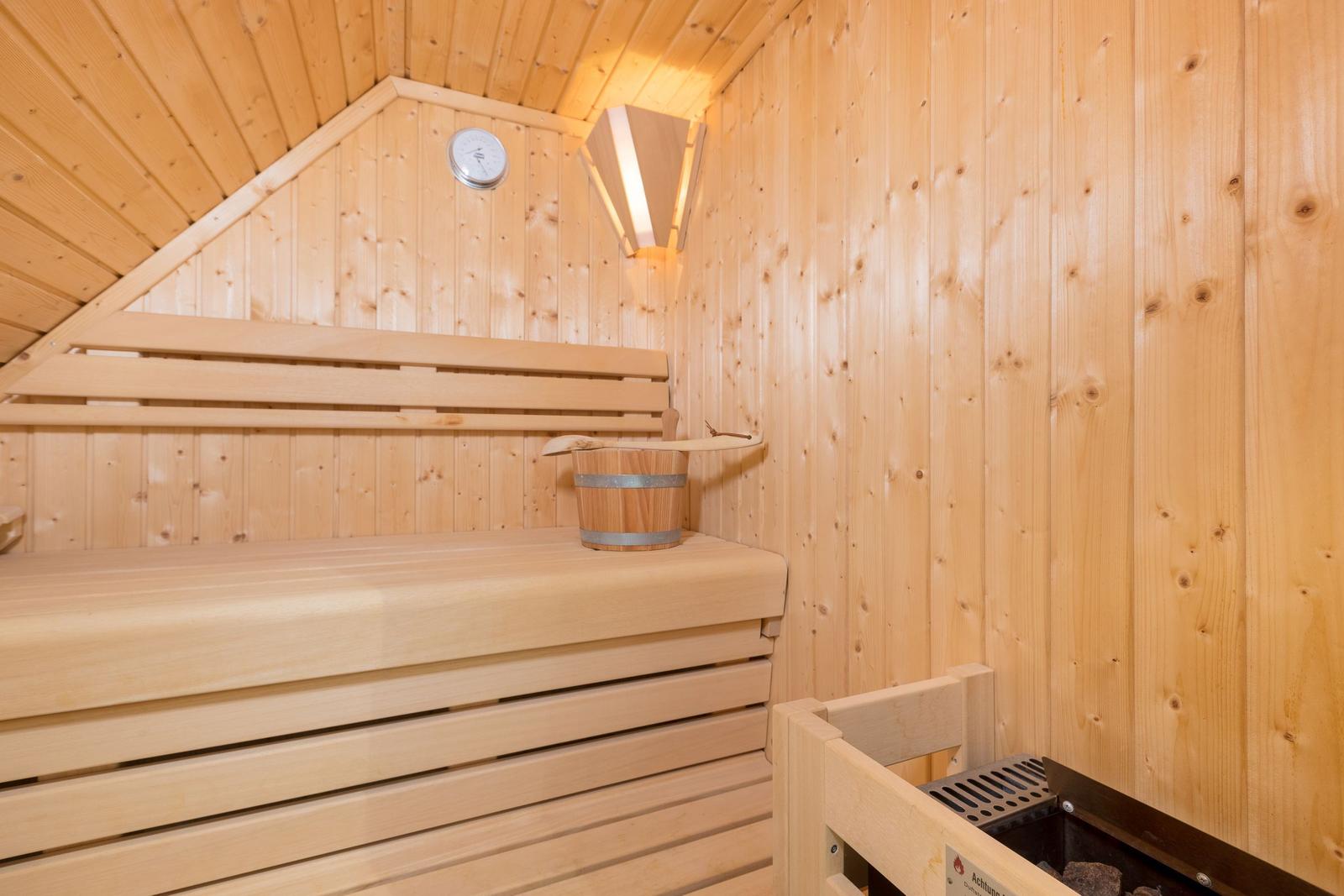 Sauna mit Holzbank, Thermometer und Eimer.