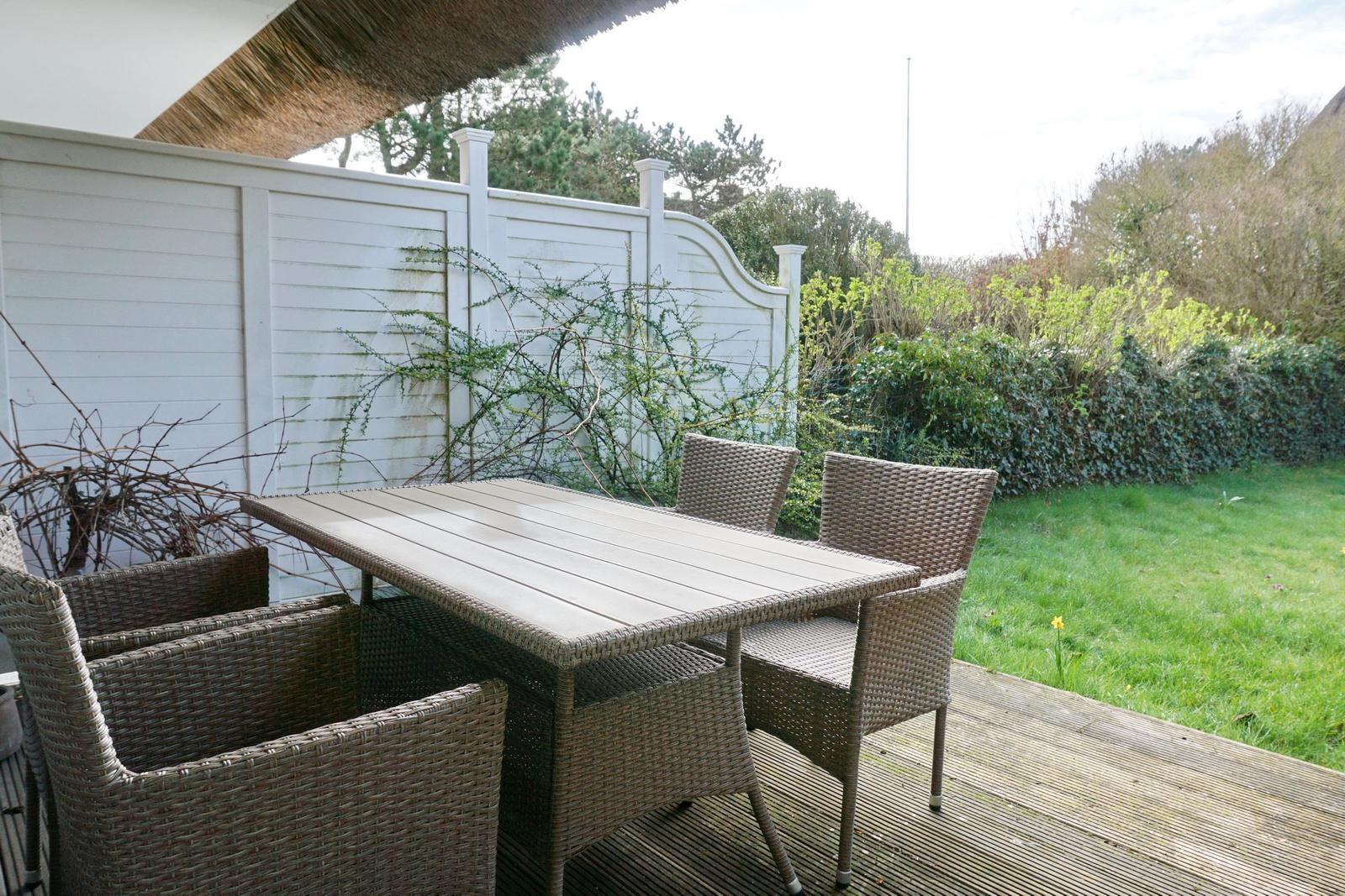 Terrasse mit Tisch und Stühlen, umgeben von Grün und weißem Zaun.