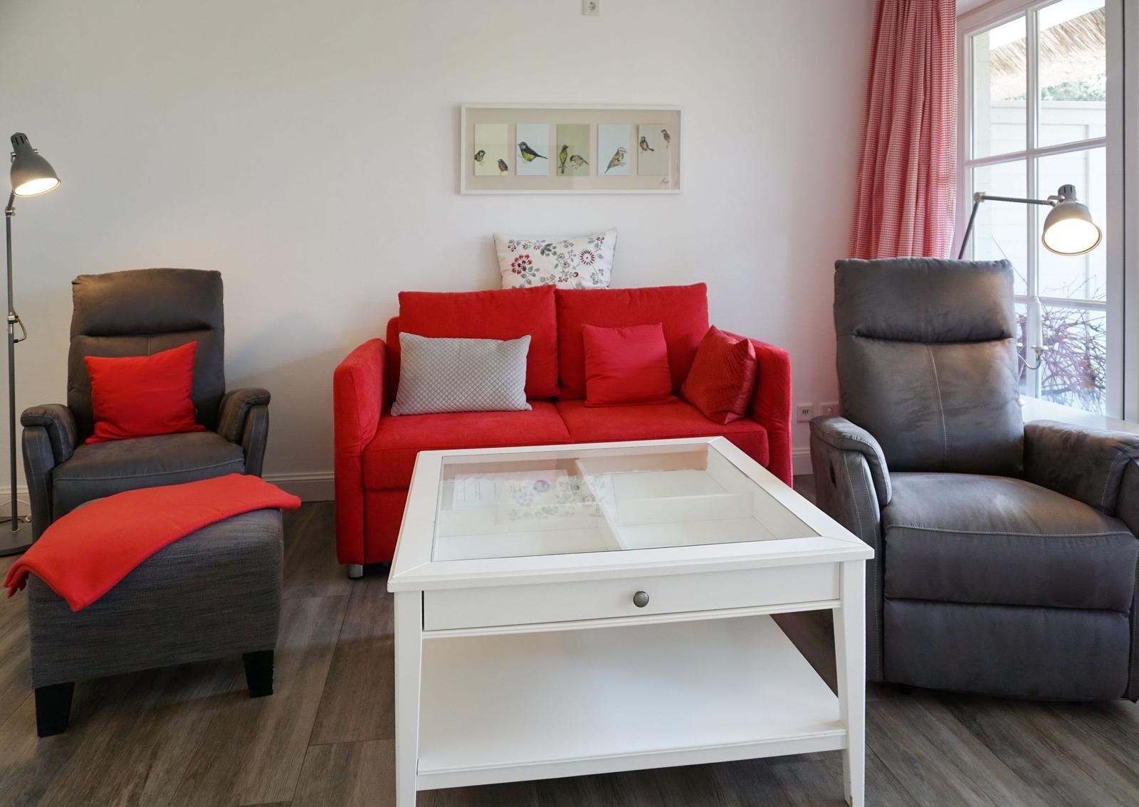 Ein Wohnzimmer mit rotem Sofa, zwei grauen Sesseln und einem weißen Couchtisch.