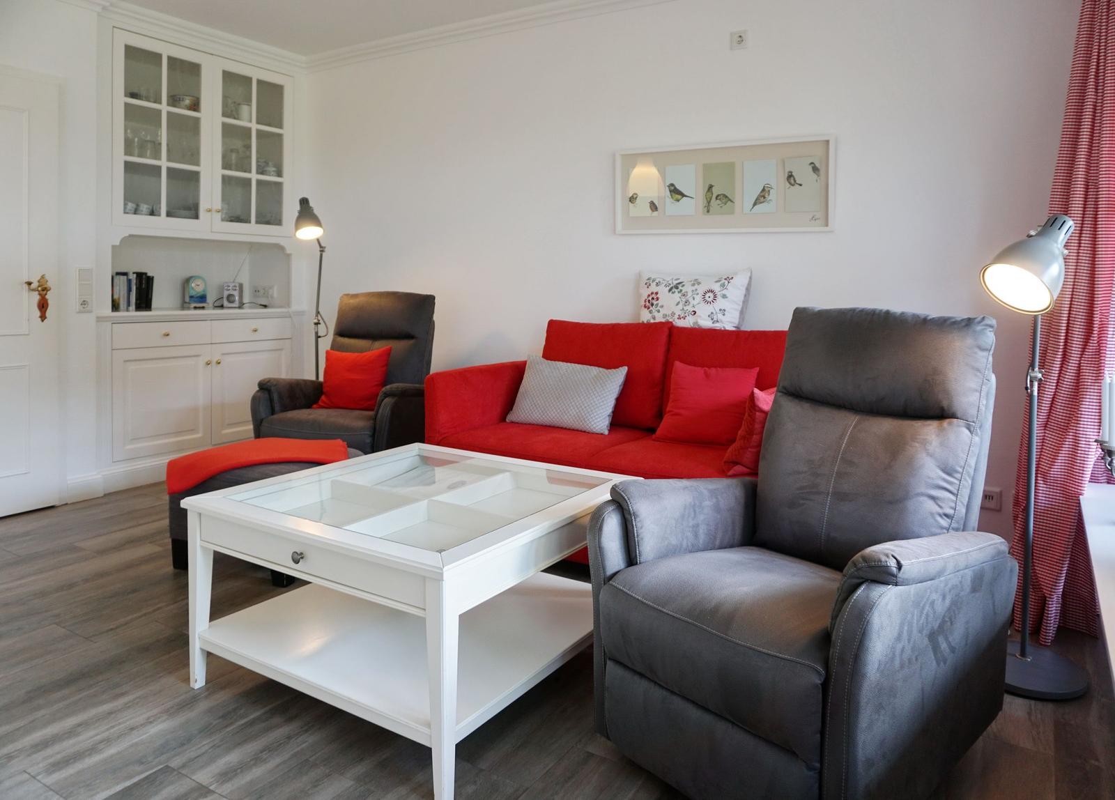 Ein Wohnzimmer mit rotem Sofa, grauen Sesseln und weißem Couchtisch.
