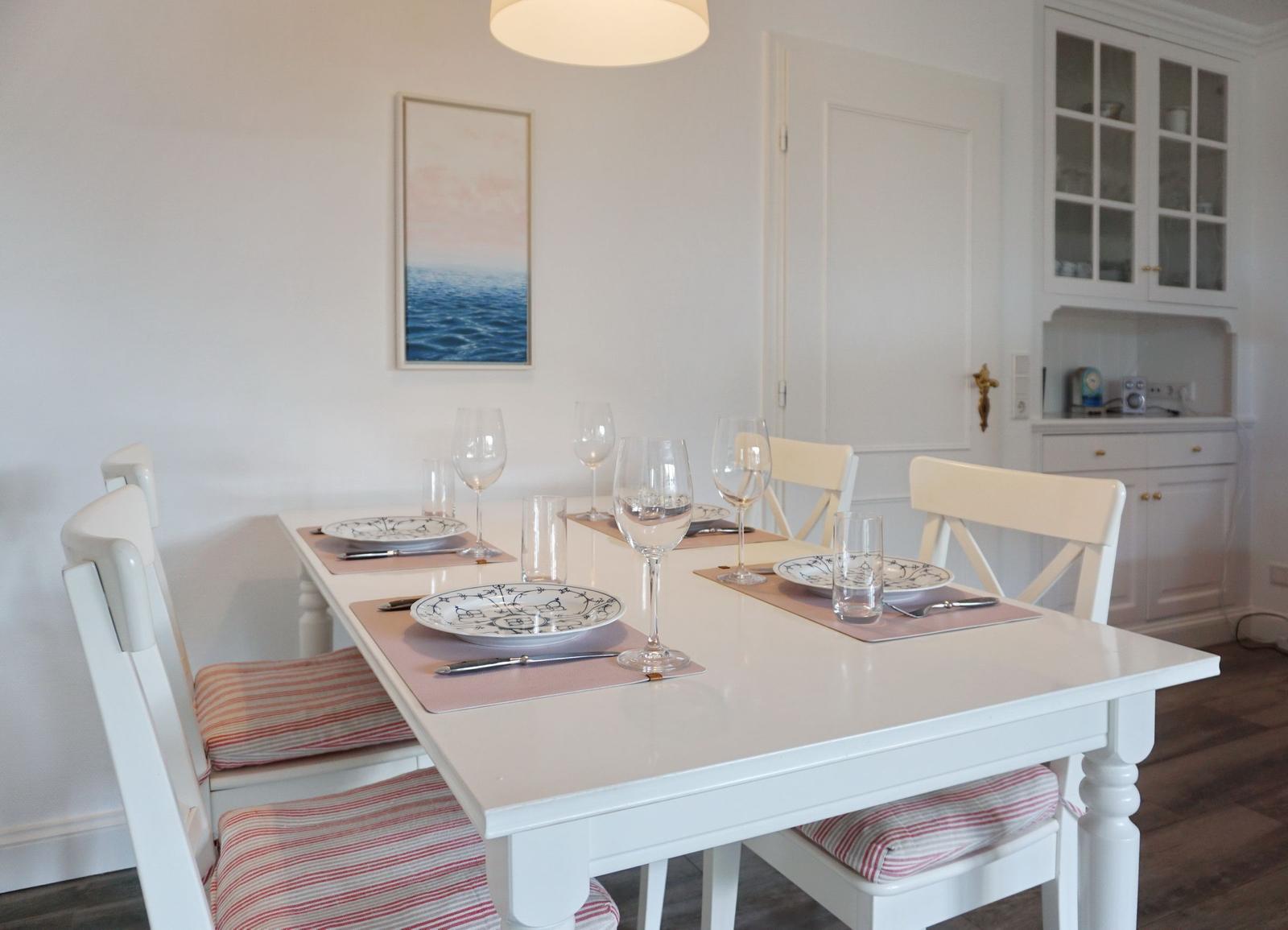 Esszimmer mit weißem Tisch, Stühlen und Platz für vier Personen.