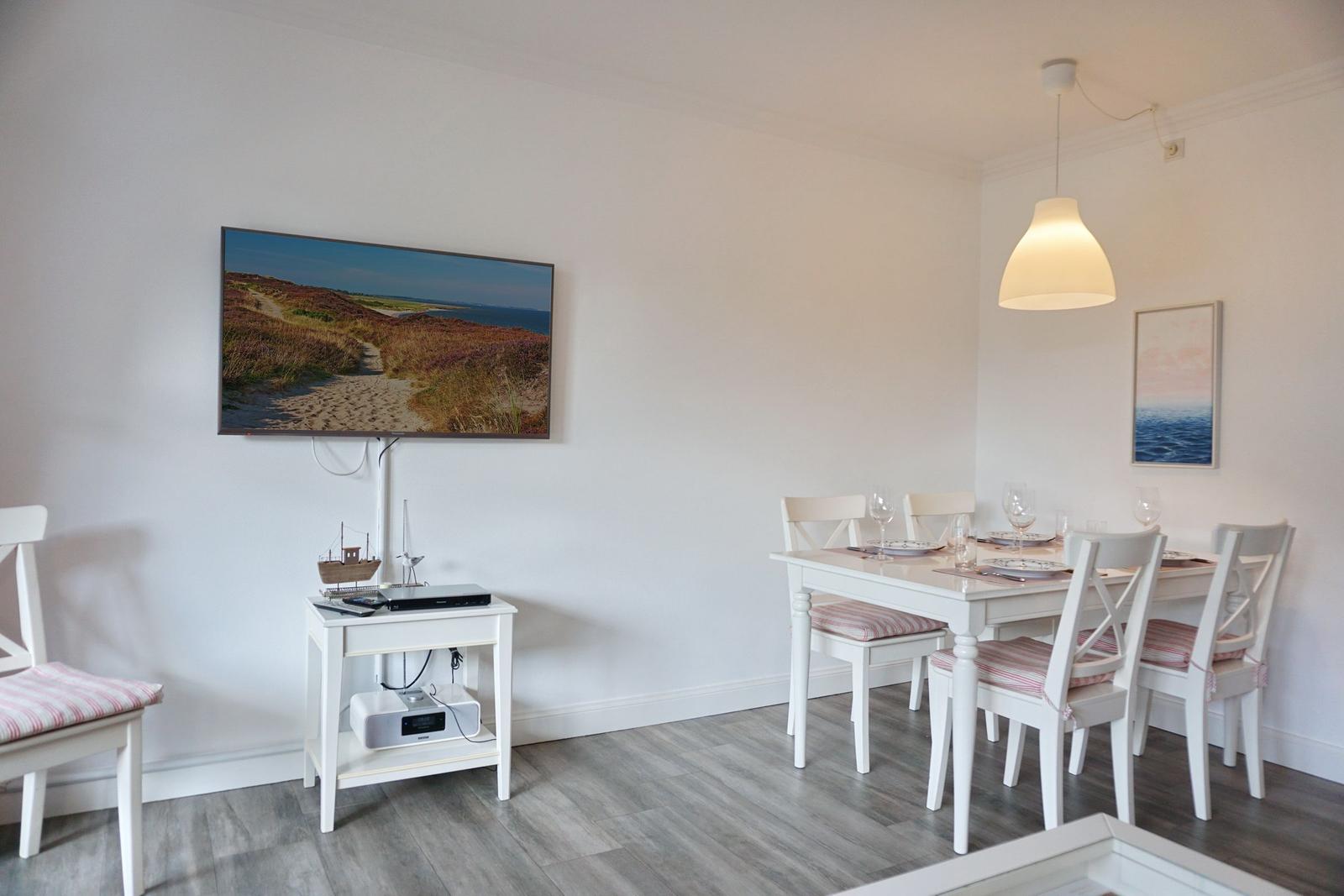 Essbereich mit weißem Tisch und Stühlen, Fernseher und Wandbild