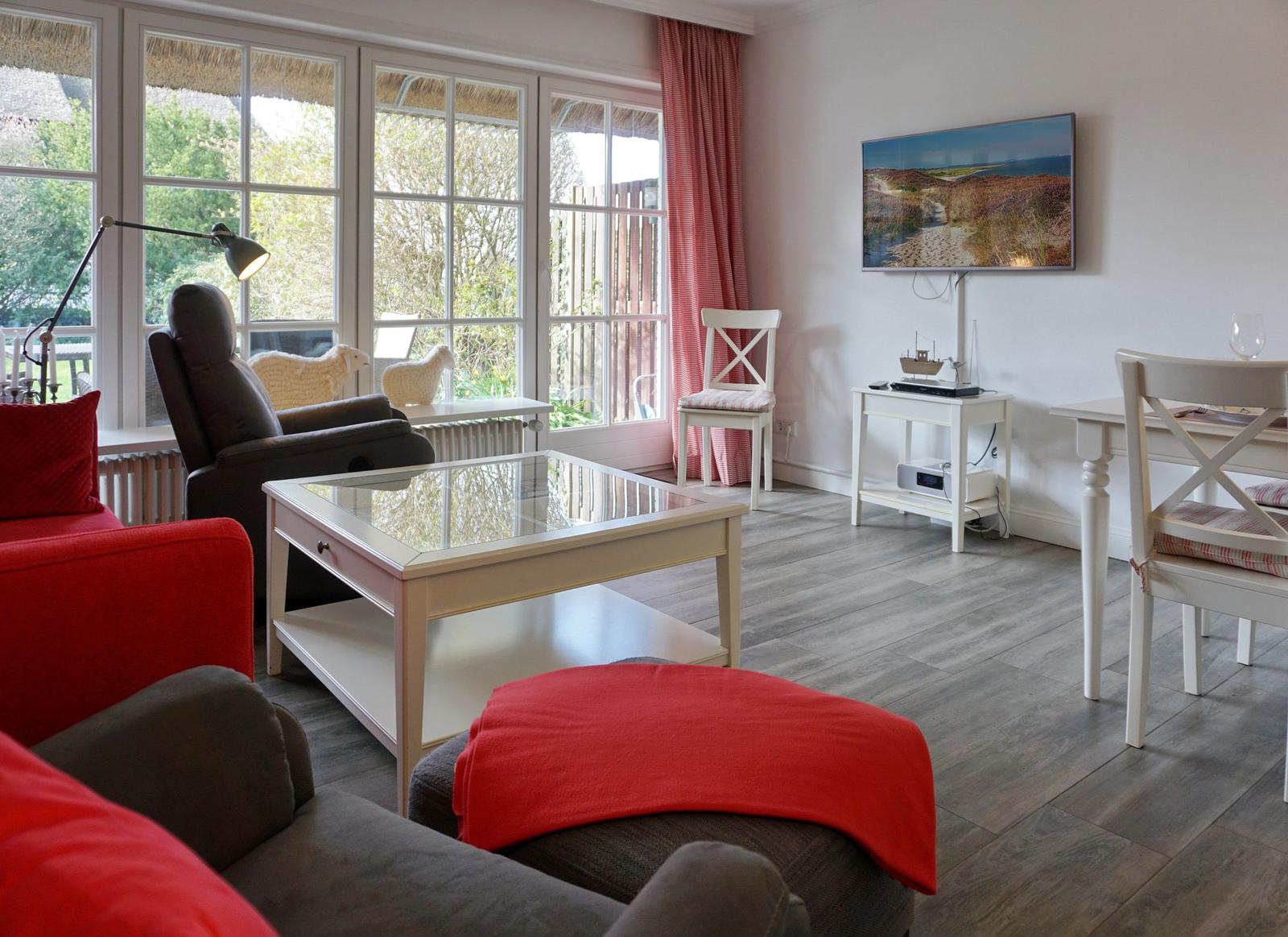 Wohnzimmer mit Glas-Tisch, roten Kissen und TV an der Wand.