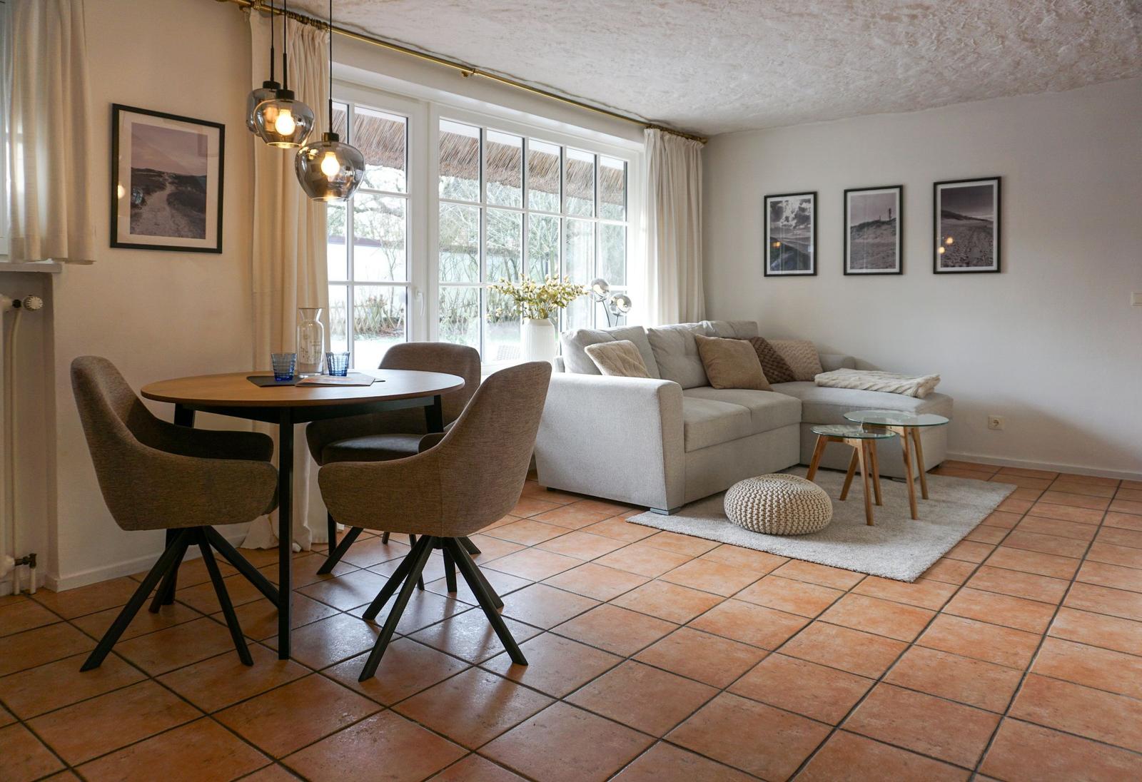 Wohn- und Essbereich mit Sofa, Tisch und Stühlen. Terrasse mit Blick durch Fenster.