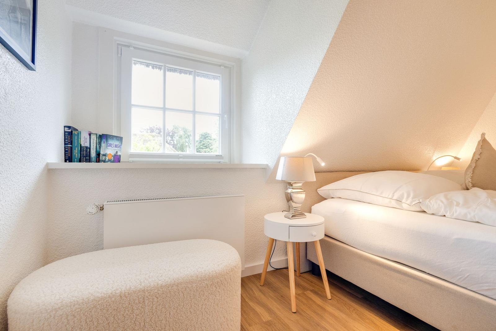 Schlafzimmer mit Bett, Nachttisch und Fenster. Bücher stehen auf der Fensterbank.