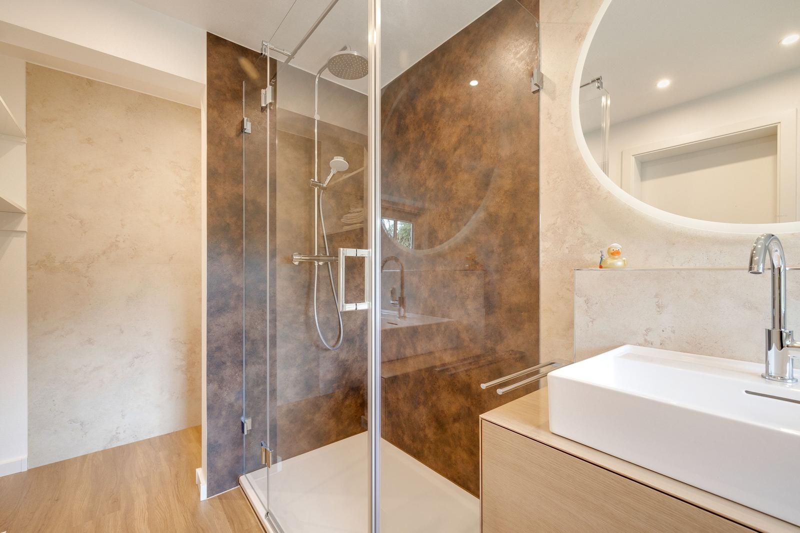Moderne Dusche mit Glaswand und Waschbecken mit runder Spiegel