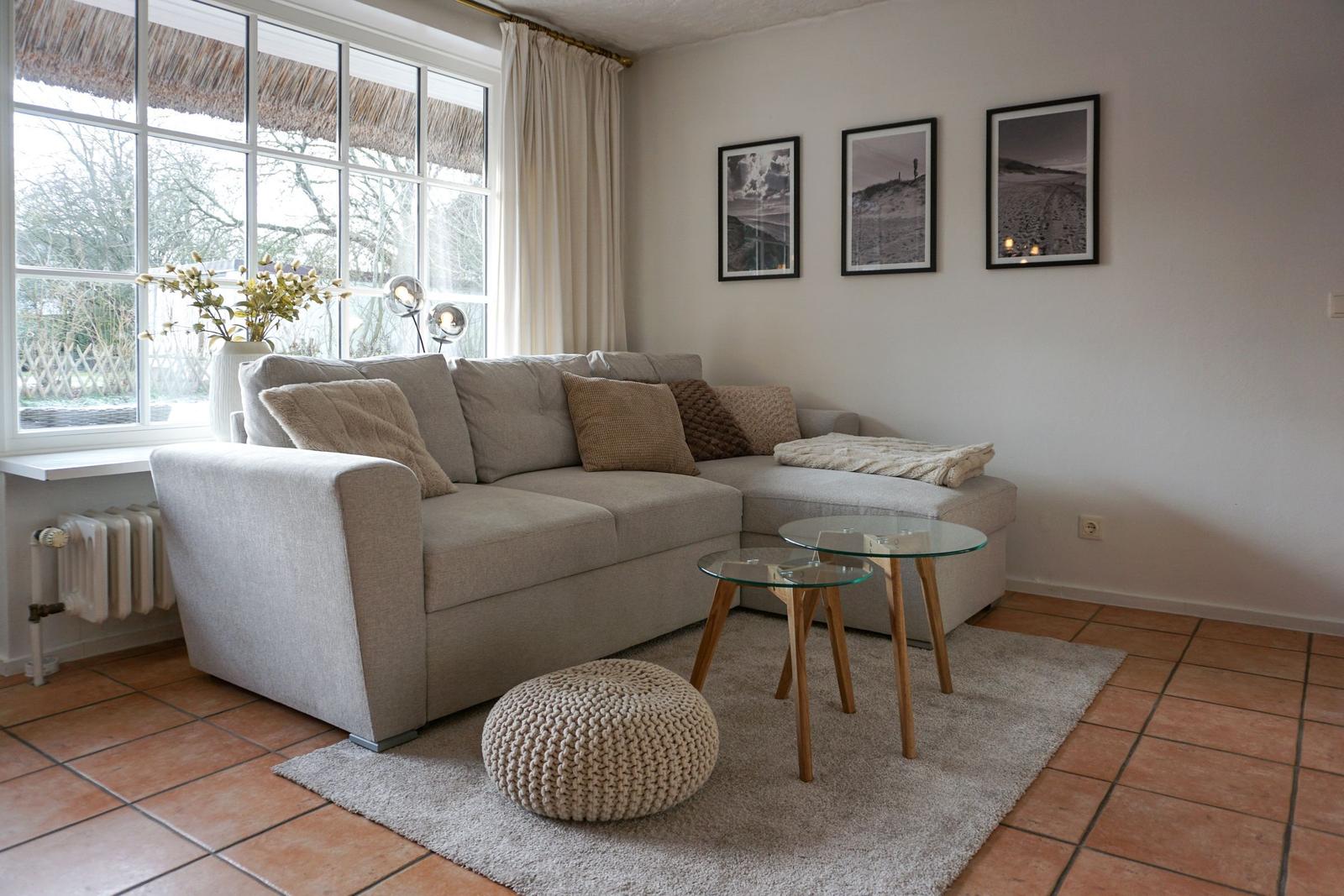 Wohnzimmer mit Eckcouch, Glas-Tischen und Fenster mit Blick nach draußen.