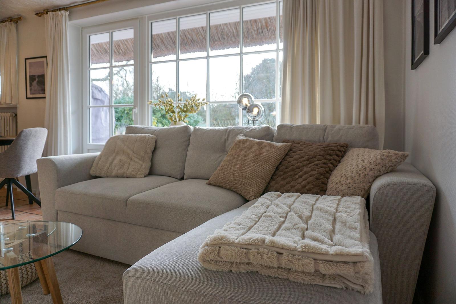Ein Sofa mit Kissen und Decke vor einem Fenster mit Blick auf die Natur.