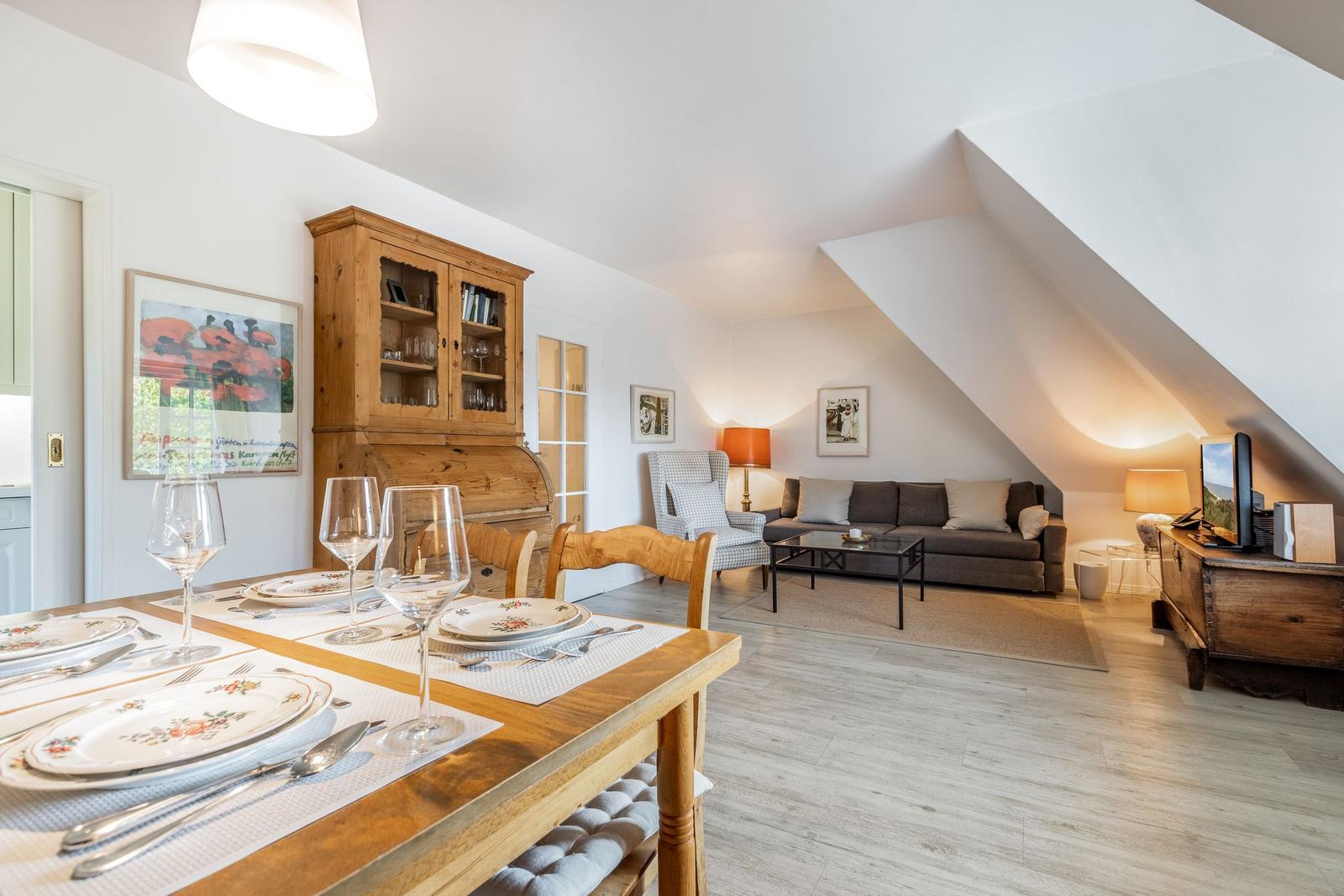Essbereich mit Tisch und Stühlen, Wohnzimmer mit Sofa und Fernseher unter Dachschrägen.