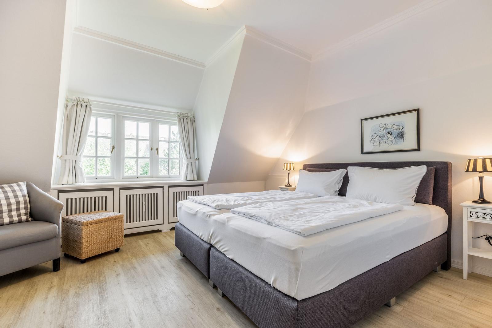 Schlafzimmer mit Doppelbett, Fenster und Sessel.