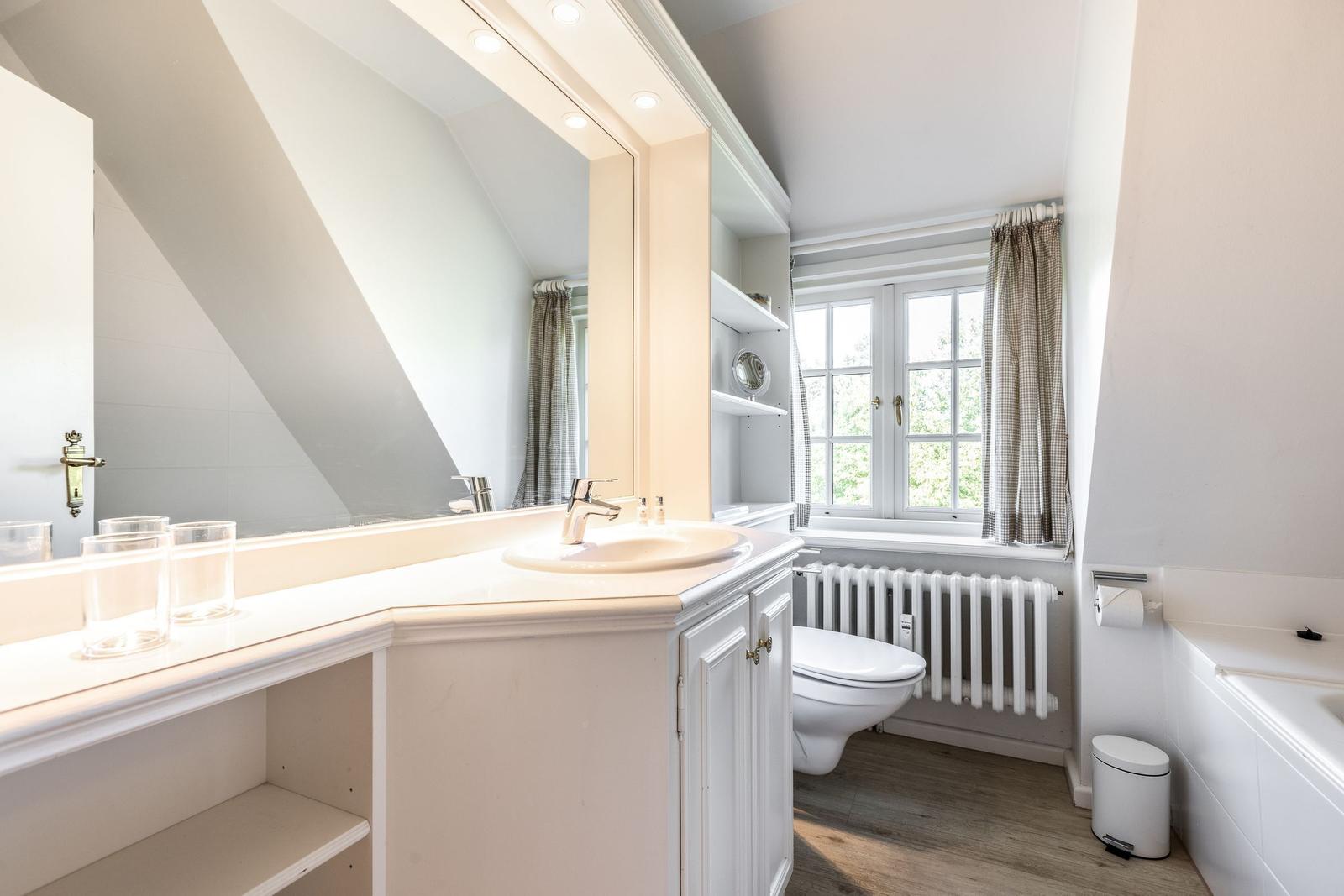Badezimmer mit Waschbecken, Spiegel, Toilette und Fenster.