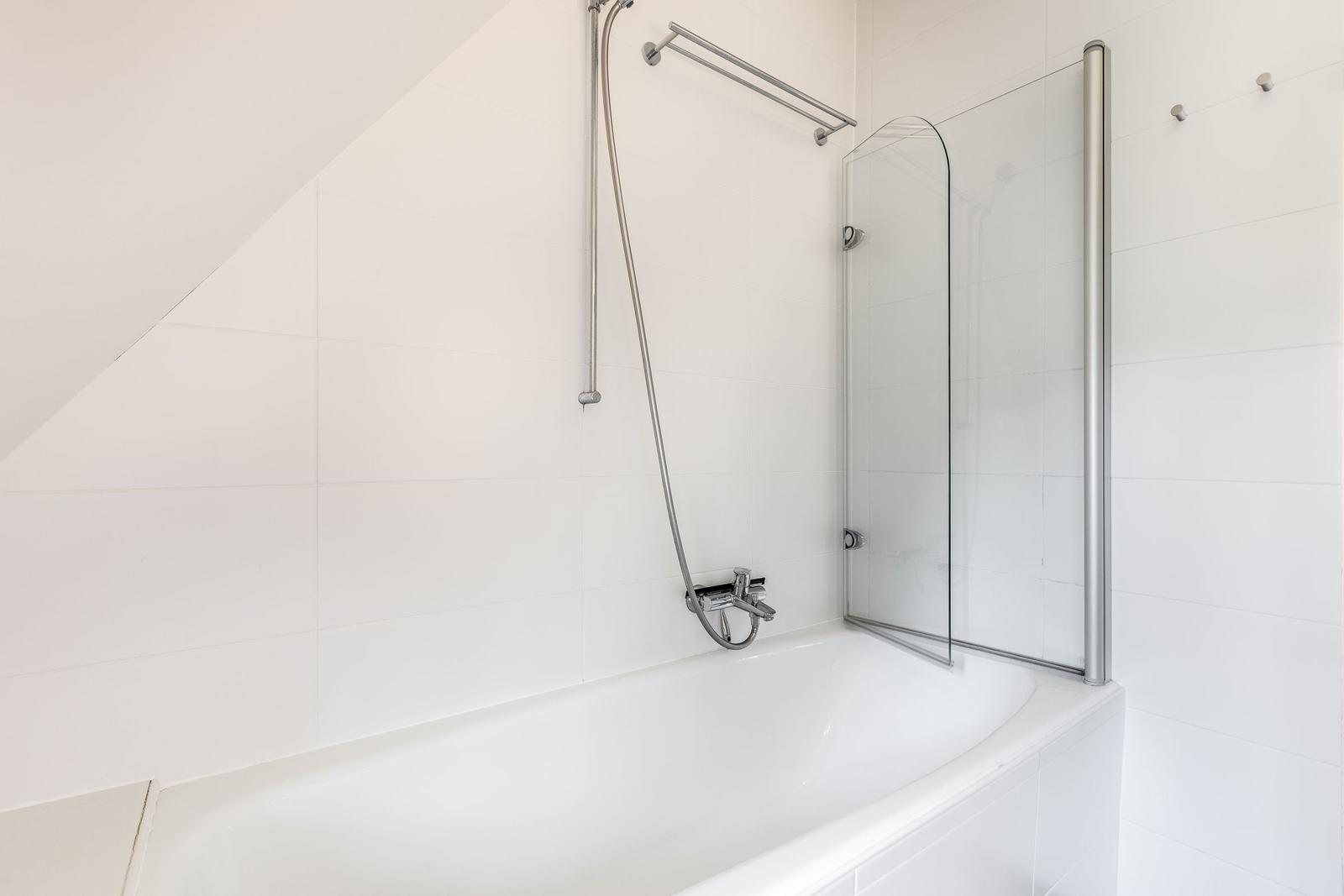 Bad mit Badewanne, Duschwand und Handbrause.