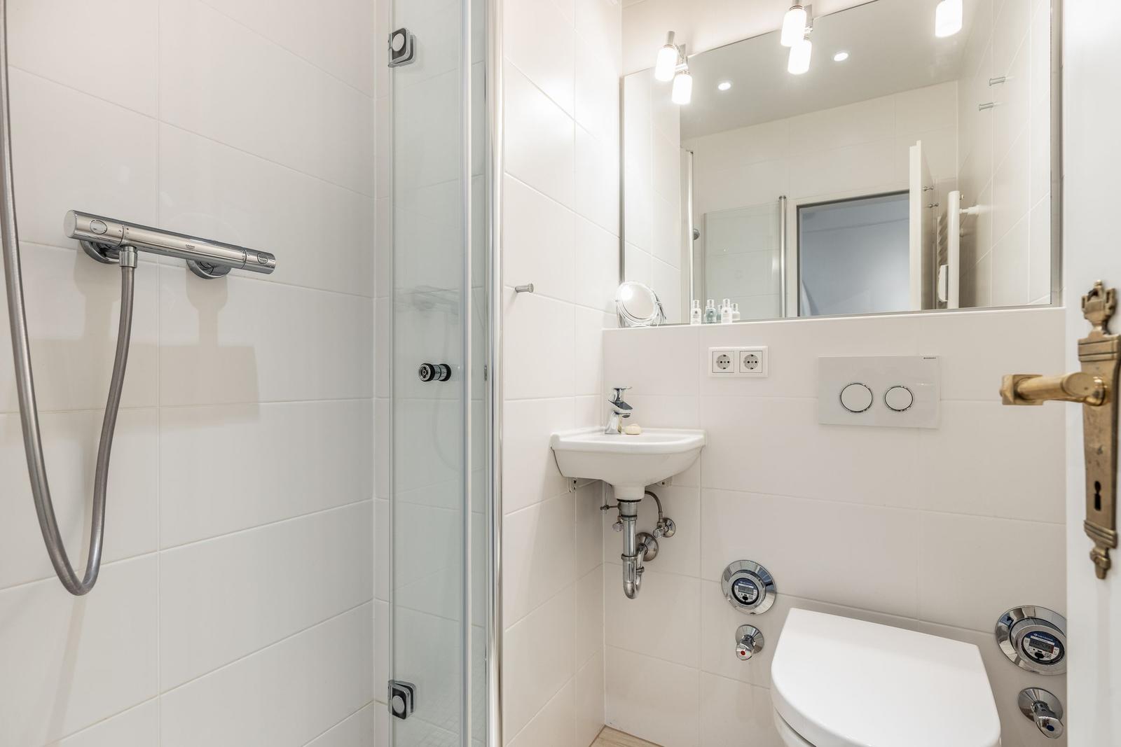 Dusche mit Duschbrause, Waschbecken und WC in weißer Ausführung.