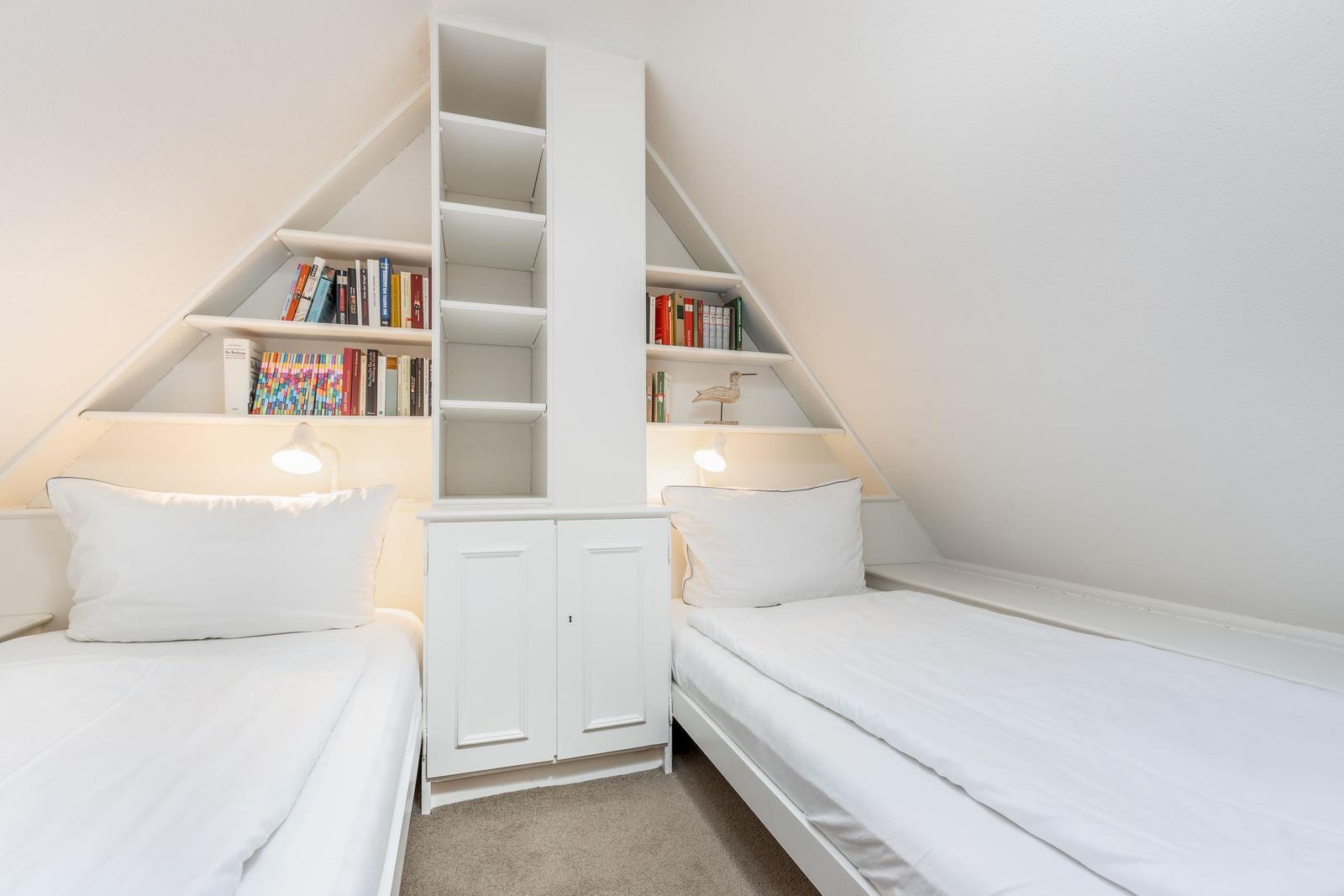 Zwei Einzelbetten unter Dachschrägen mit Bücherregalen und Nachttisch