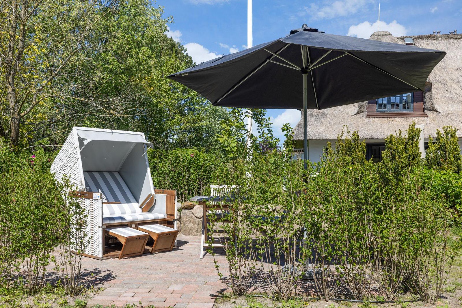 Terrasse mit Strandkorb, Sonnenschirm und Gartenhaus im Hintergrund.